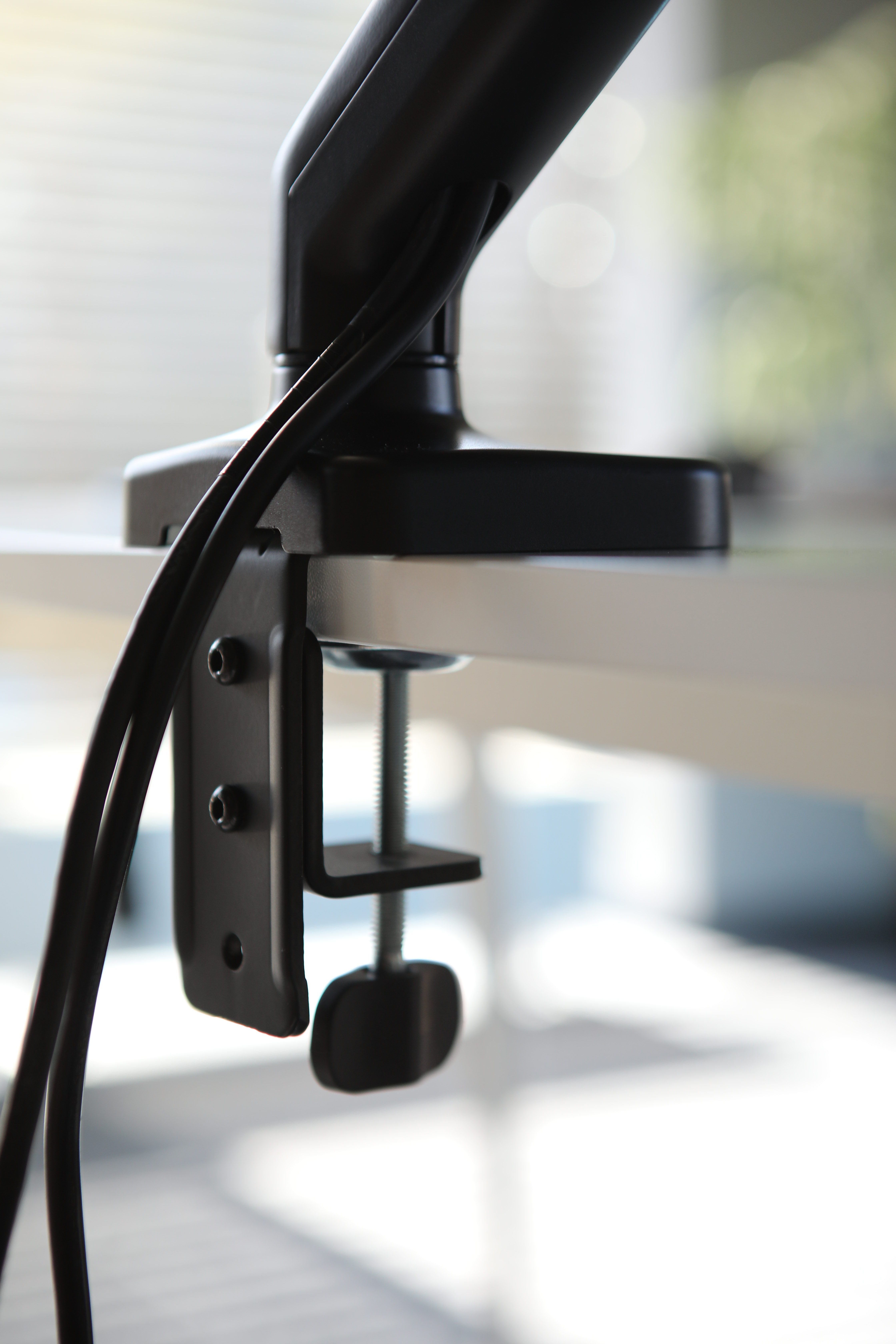 Czarny ramię zacisku biurkowego z kablami przymocowanymi do białej powierzchni.