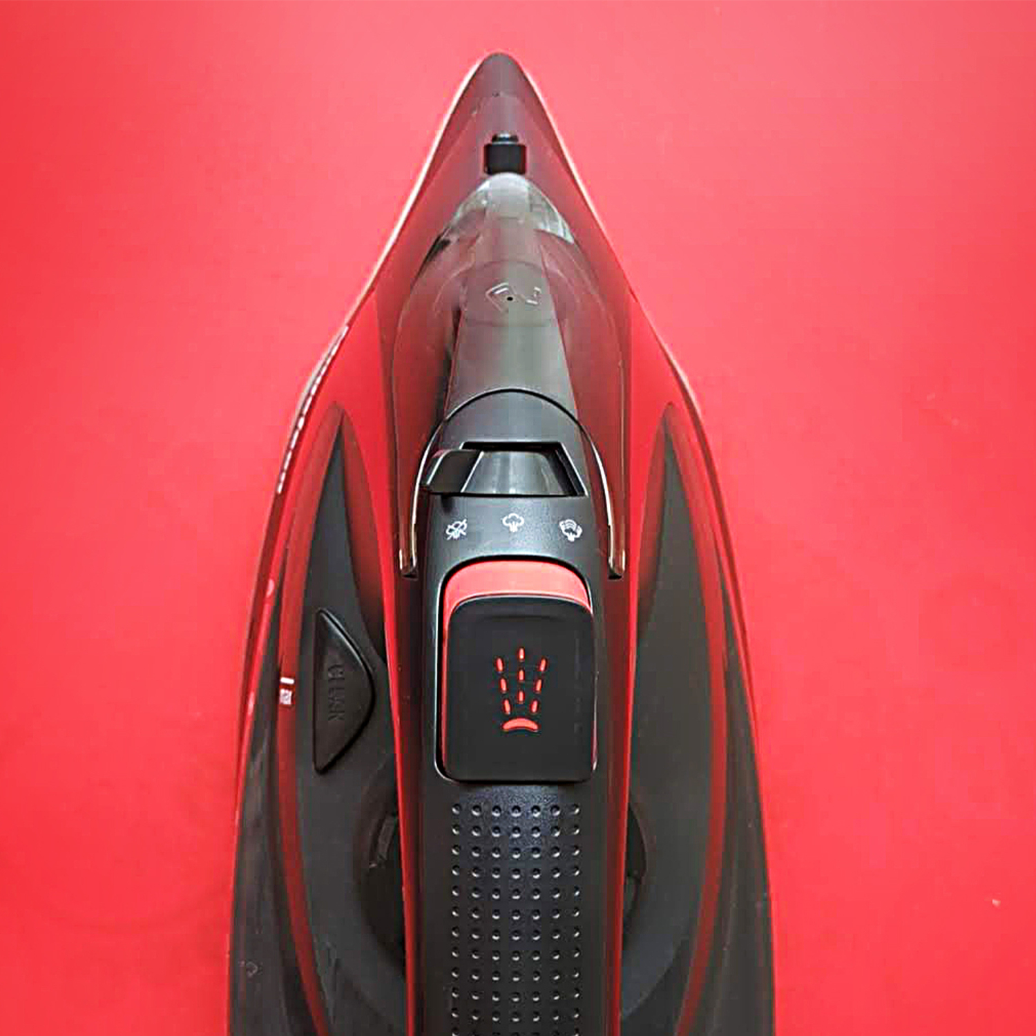 Vista superior de una plancha de vapor negra con detalles rojos sobre fondo rojo.