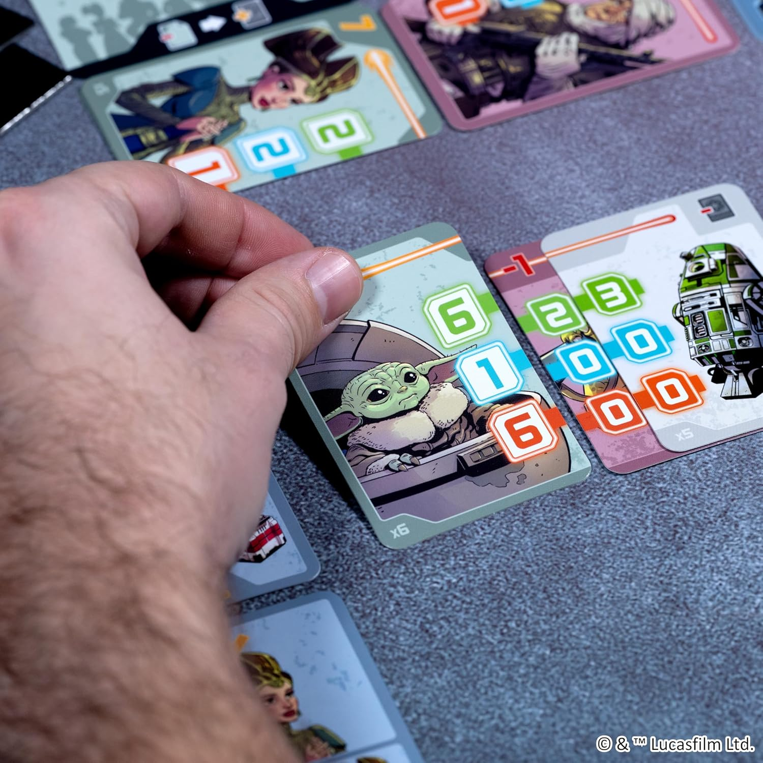 Hand hält Baby Yoda Karte über Spielkarten mit Zahlen und Charakteren.