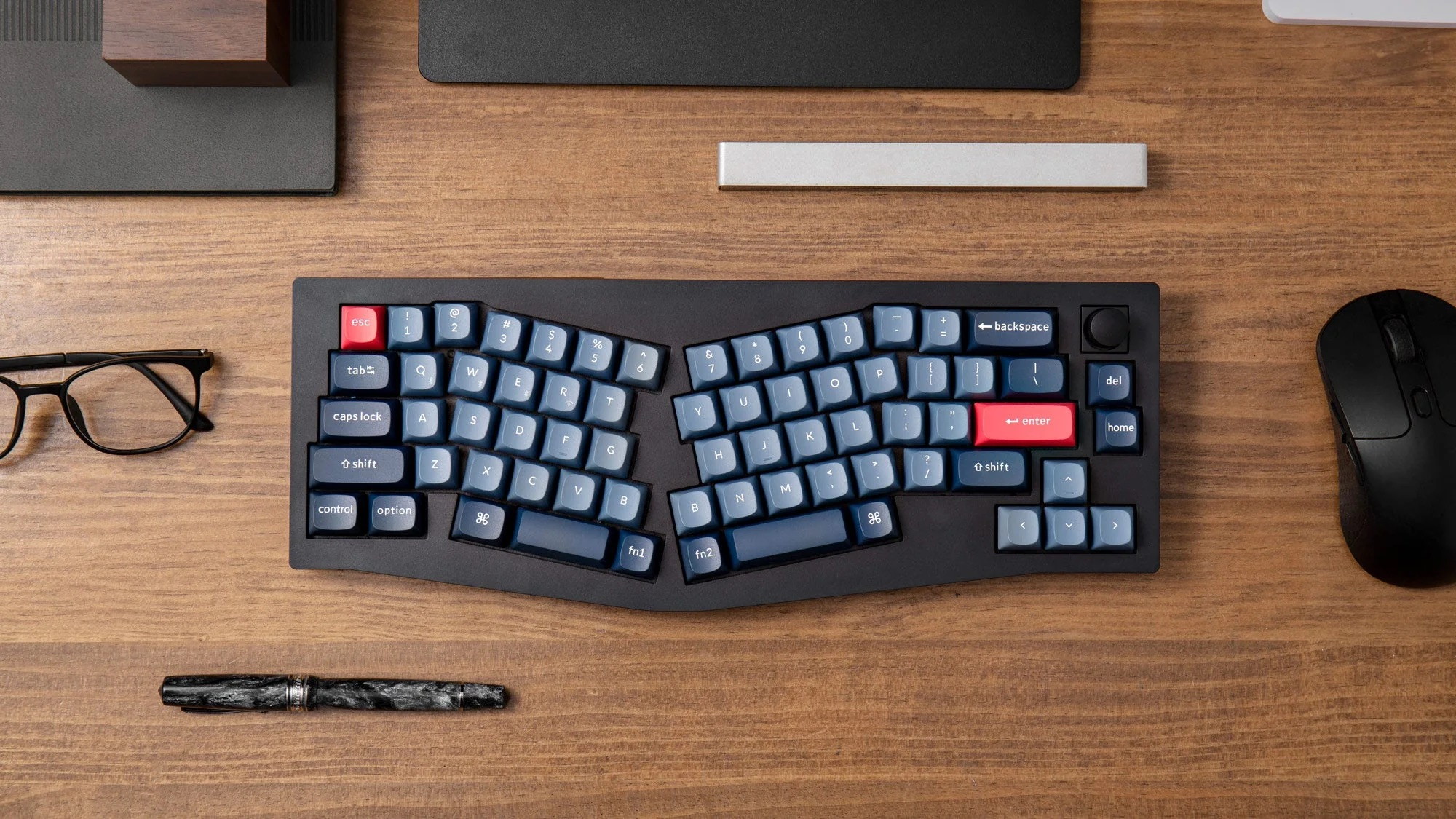 Dzielona klawiatura ergonomiczna z niebieskimi klawiszami, czerwonymi klawiszami ESC i Enter, na drewnianym biurku.