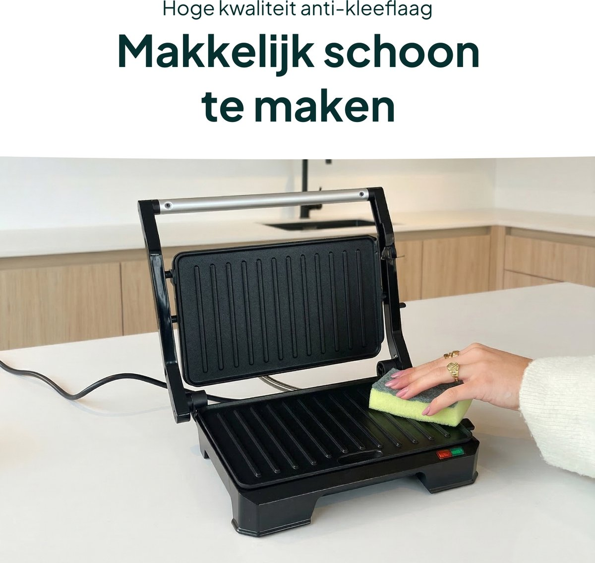A hand cleans a black contact grill with a green sponge.