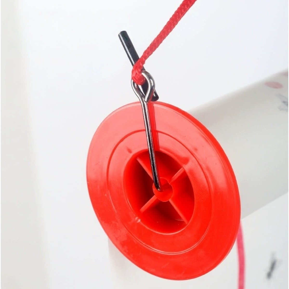 Bobina di plastica rossa con spillo metallico e filo rosso su tubo bianco.