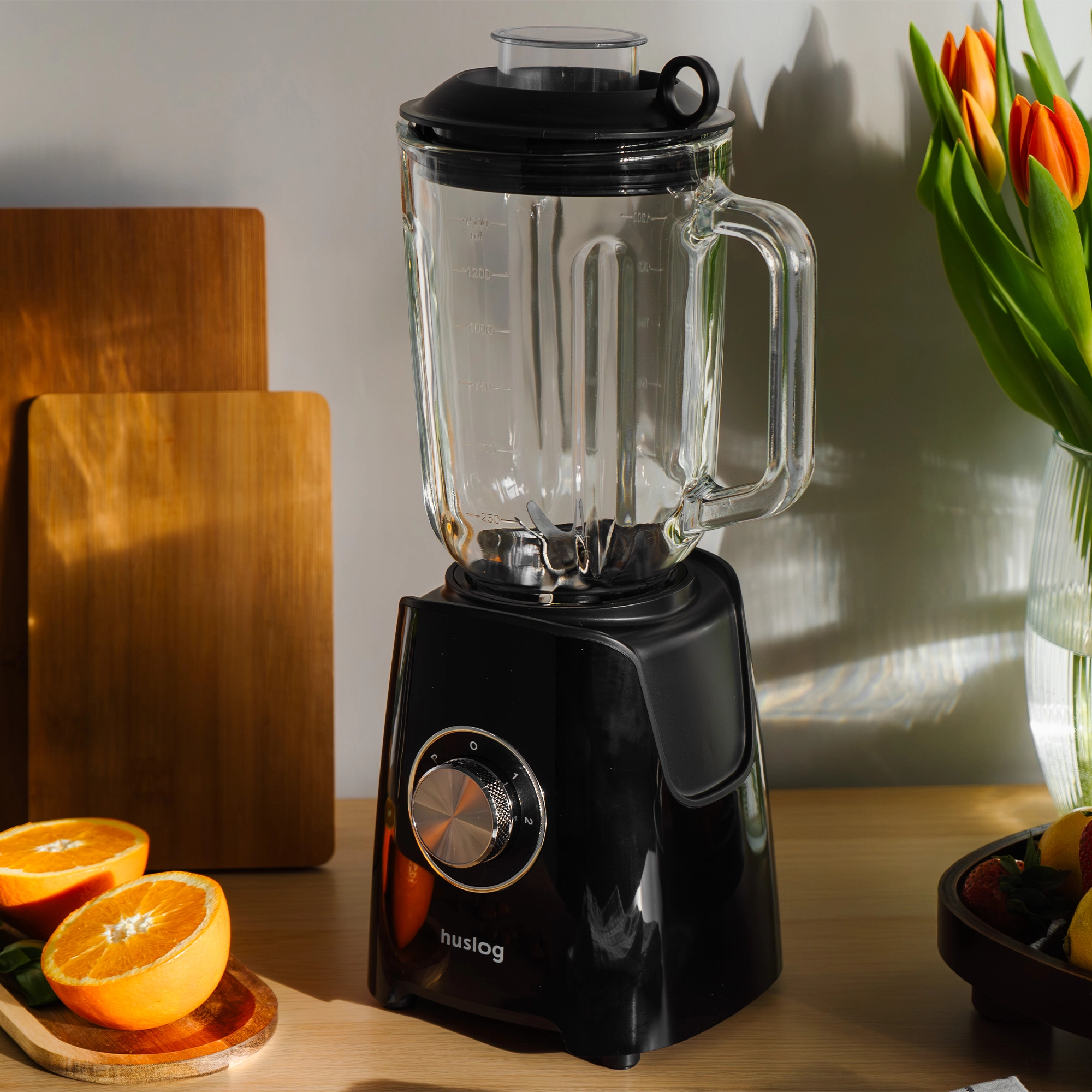 Czarny blender ze szklanym dzbankiem, pomarańczami, drewnianymi deskami i tulipanami.