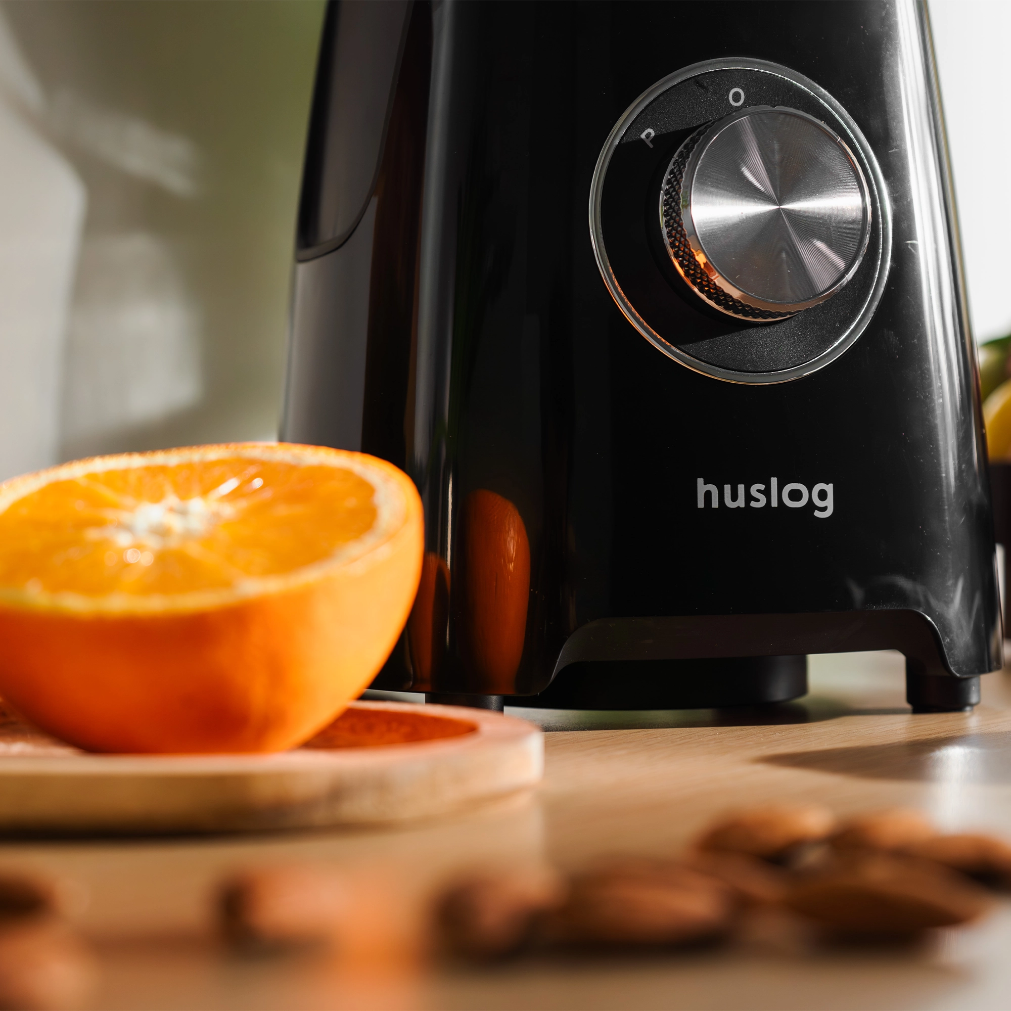 Czarny blender Huslog z połówką pomarańczy i migdałami.