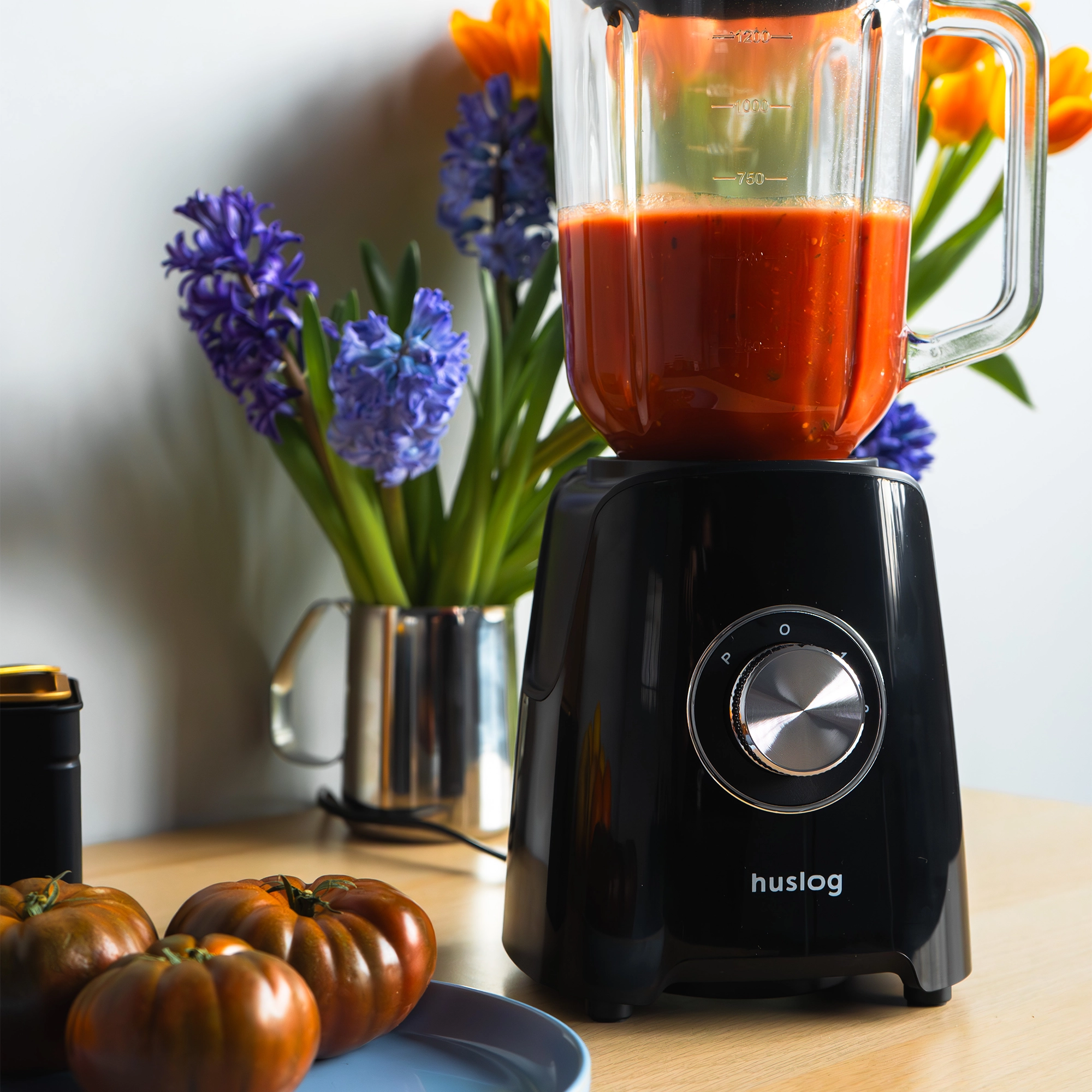 Czarny blender z czerwonym płynem i kwiatami w tle.
