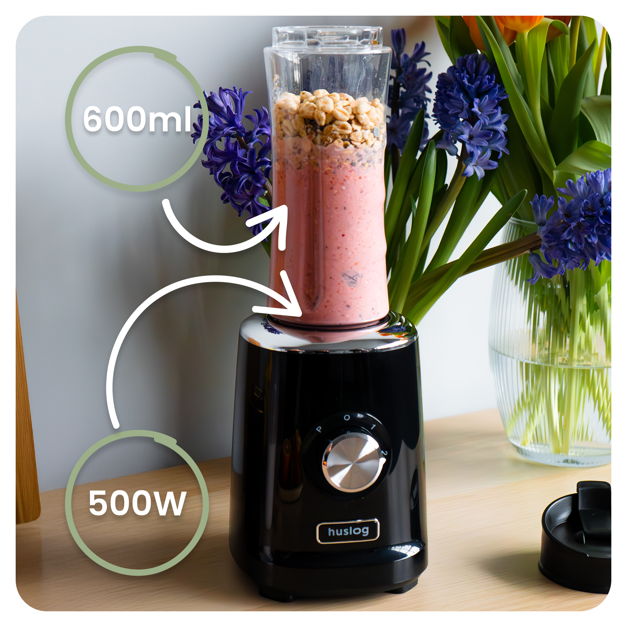 Czarny blender z kubkiem 600ml wypełnionym smoothie i płatkami. Kwiaty w tle.