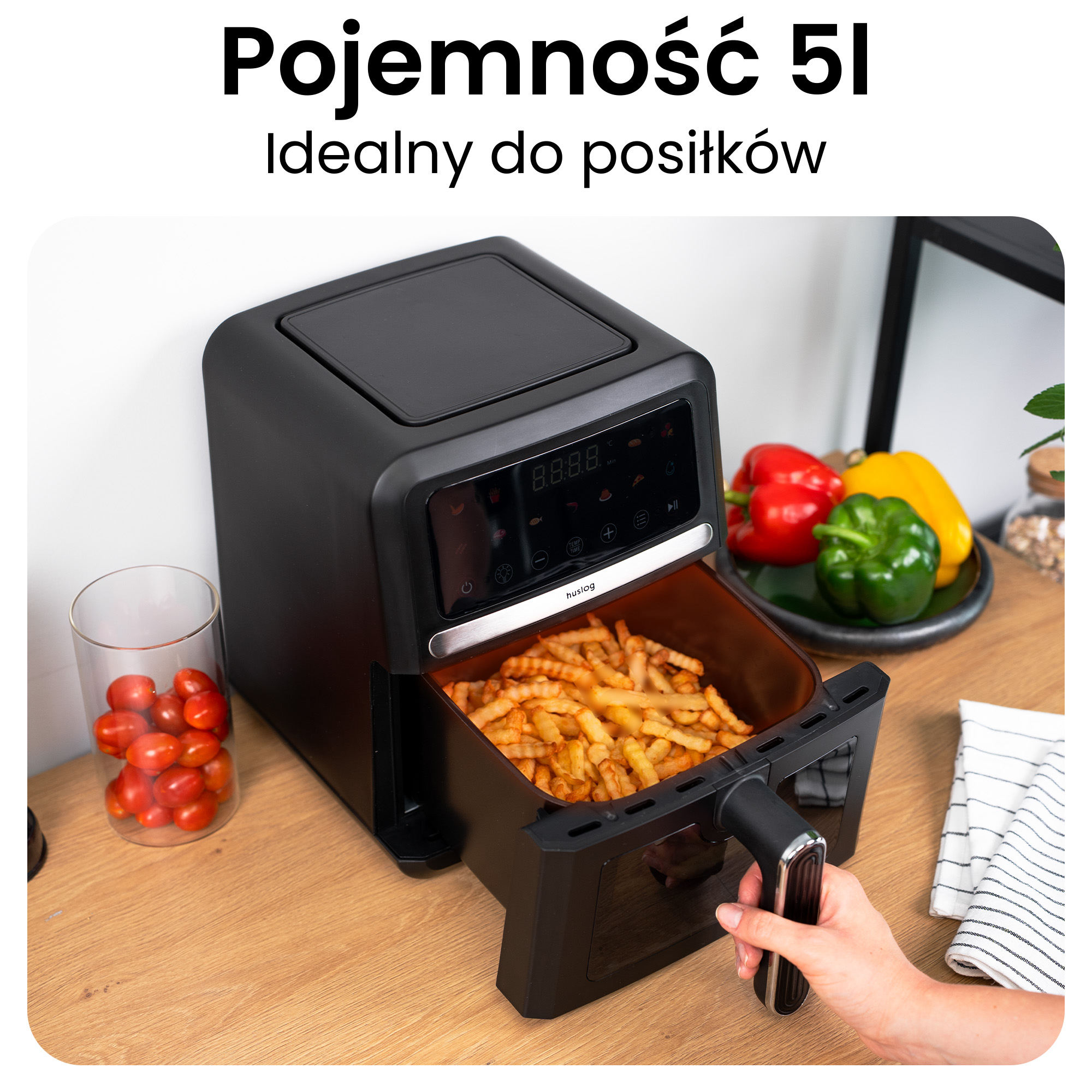 Czarna frytkownica beztłuszczowa z frytkami, pomidorami i papryką na drewnianym stole.