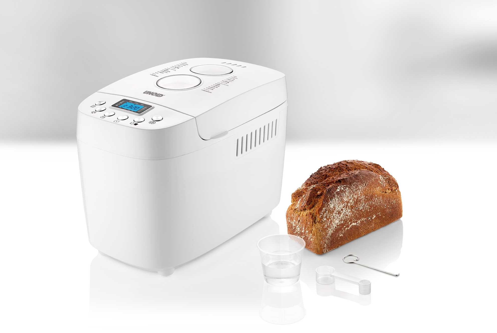 Ein weißer Brotbackautomat mit Brot, Messbecher und Werkzeug.