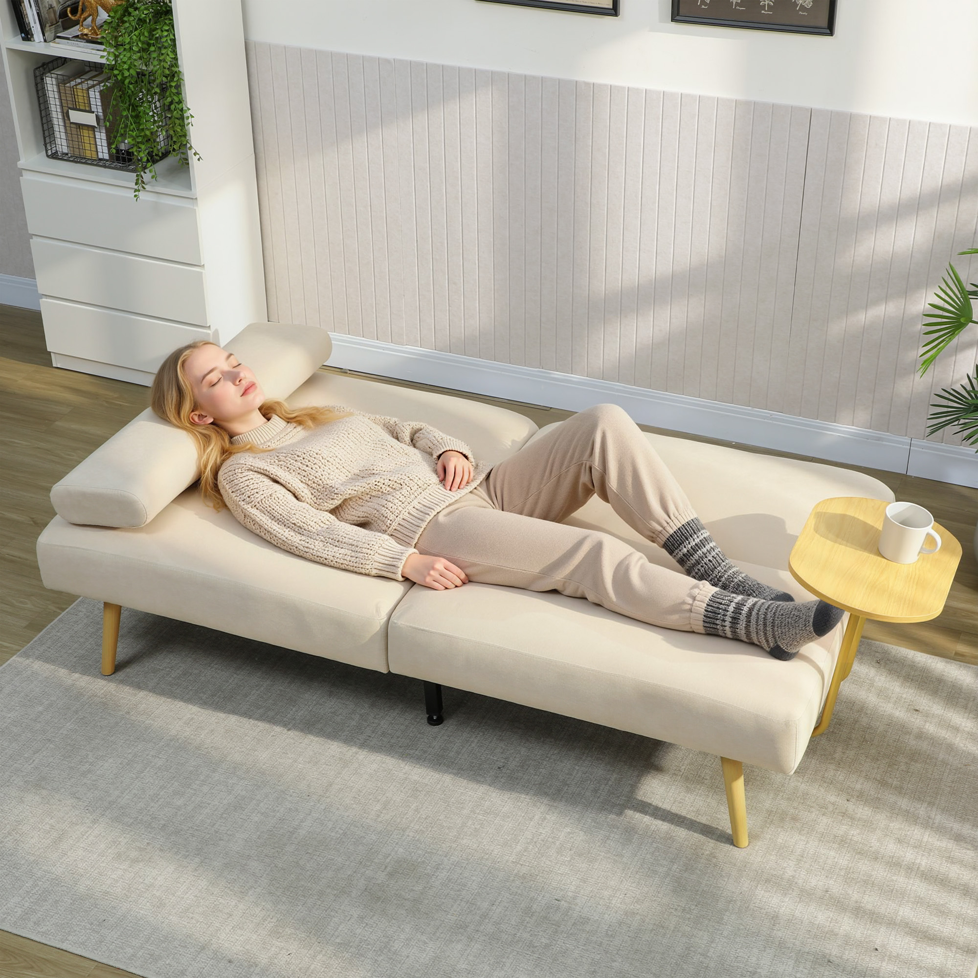 Una mujer duerme en un sofá color crema, junto a una mesita de madera con una taza.