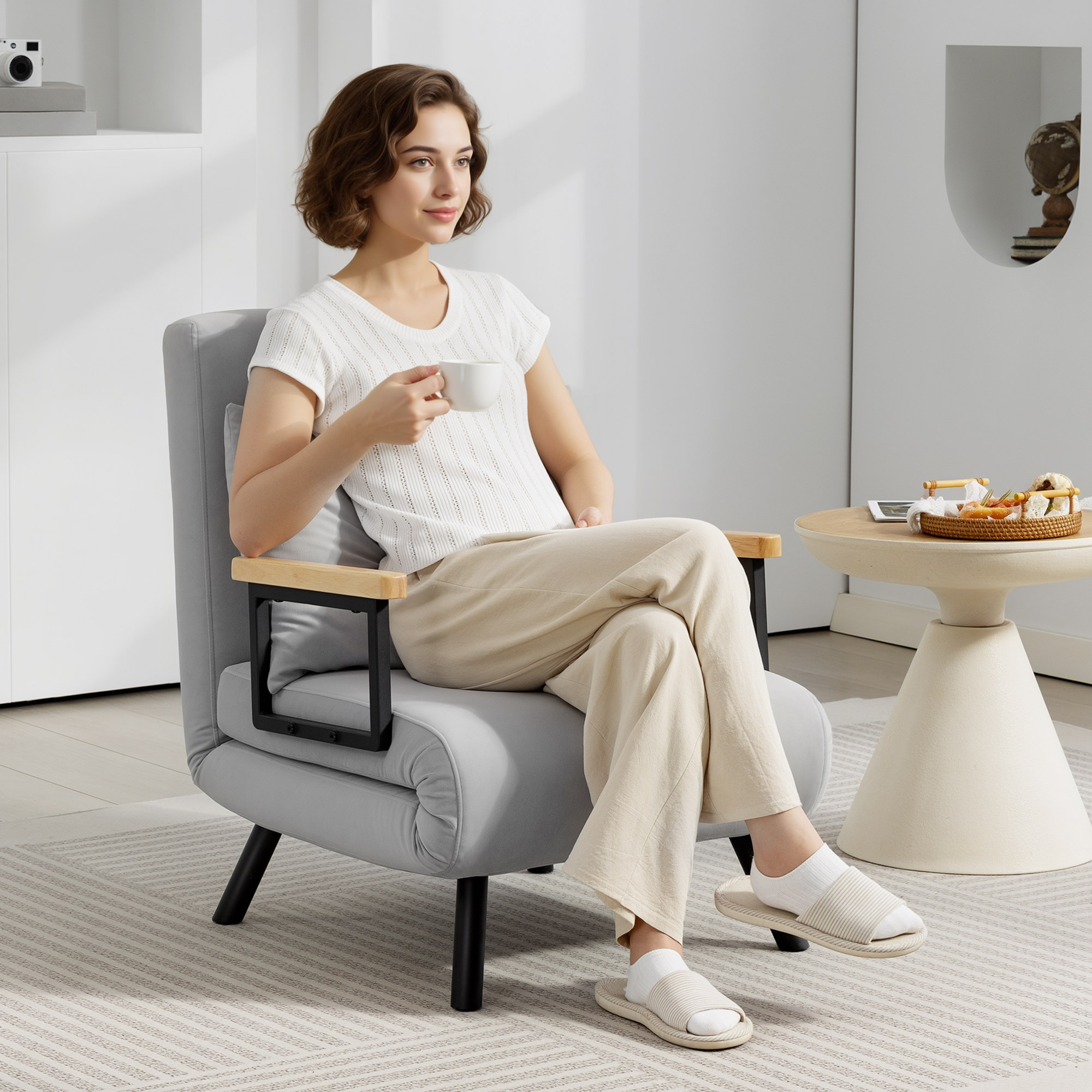 Una mujer sentada en un sillón gris, sosteniendo una taza de café. Una mesita auxiliar cerca.