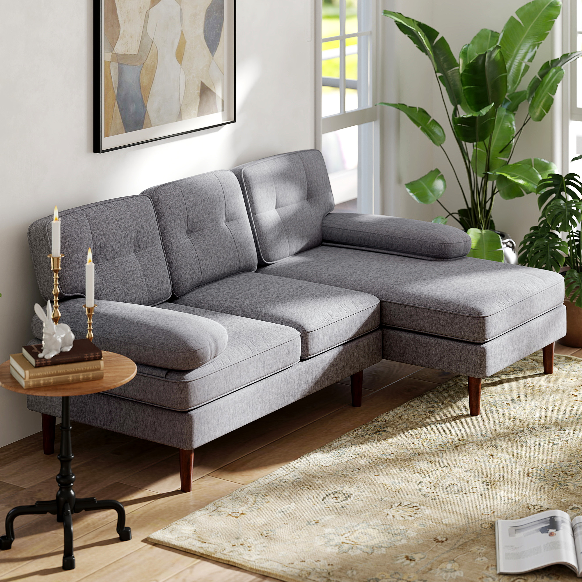 Un sofá seccional gris con mesa de madera, velas, arte y plantas.