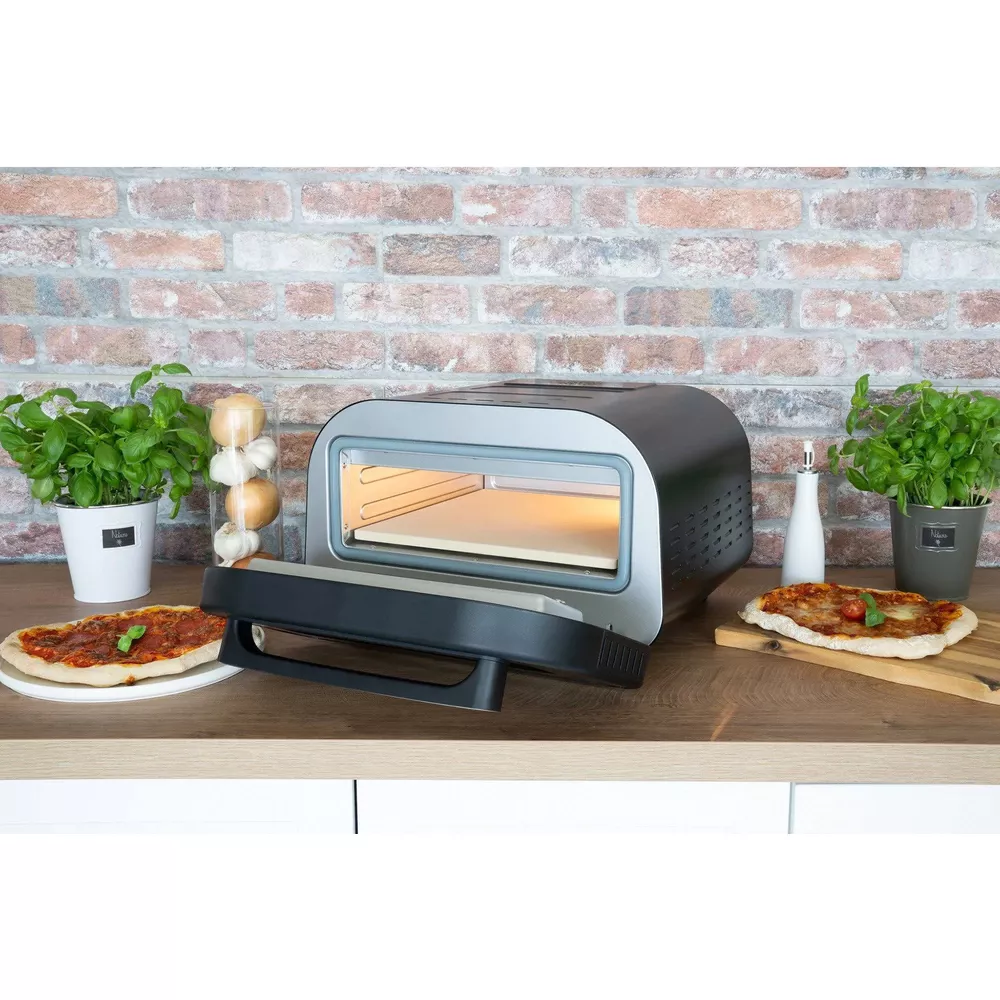 Ein Pizzaofen steht auf einer Arbeitsplatte mit zwei Pizzen, Basilikum und Knoblauch.