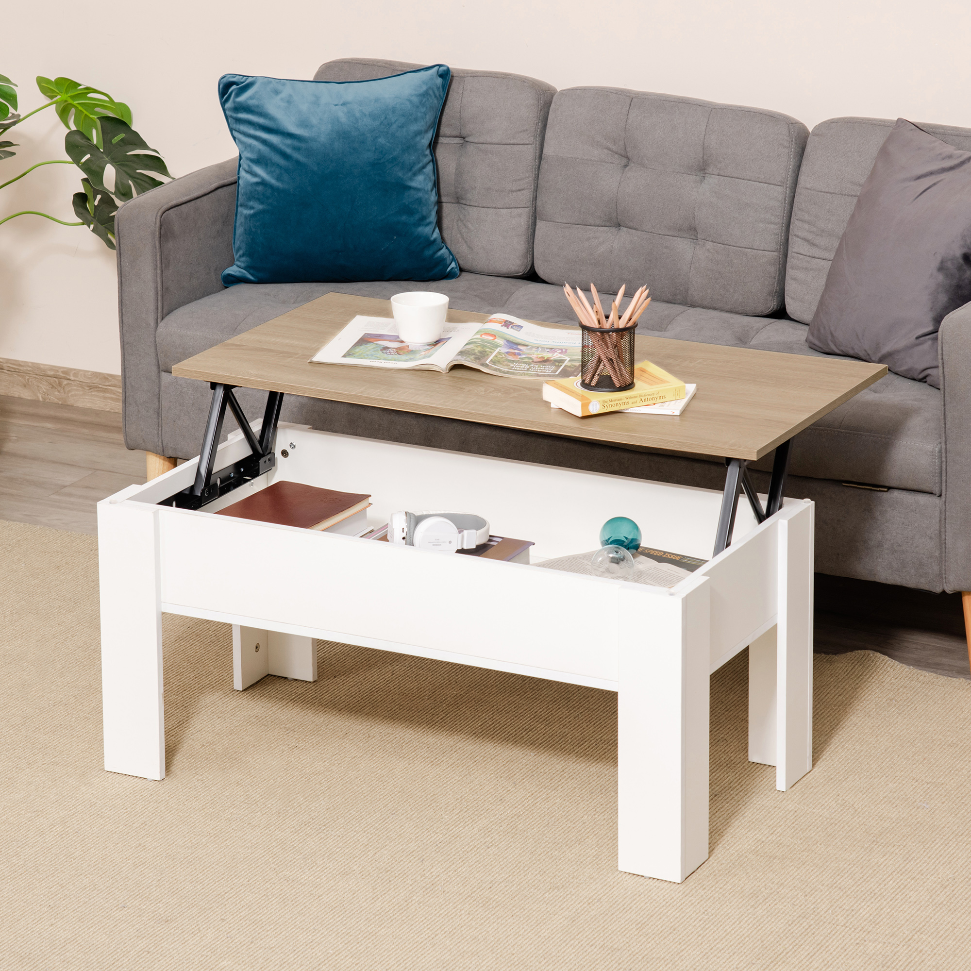 Una mesa de centro elevable, de madera y blanca, con libros y auriculares dentro.