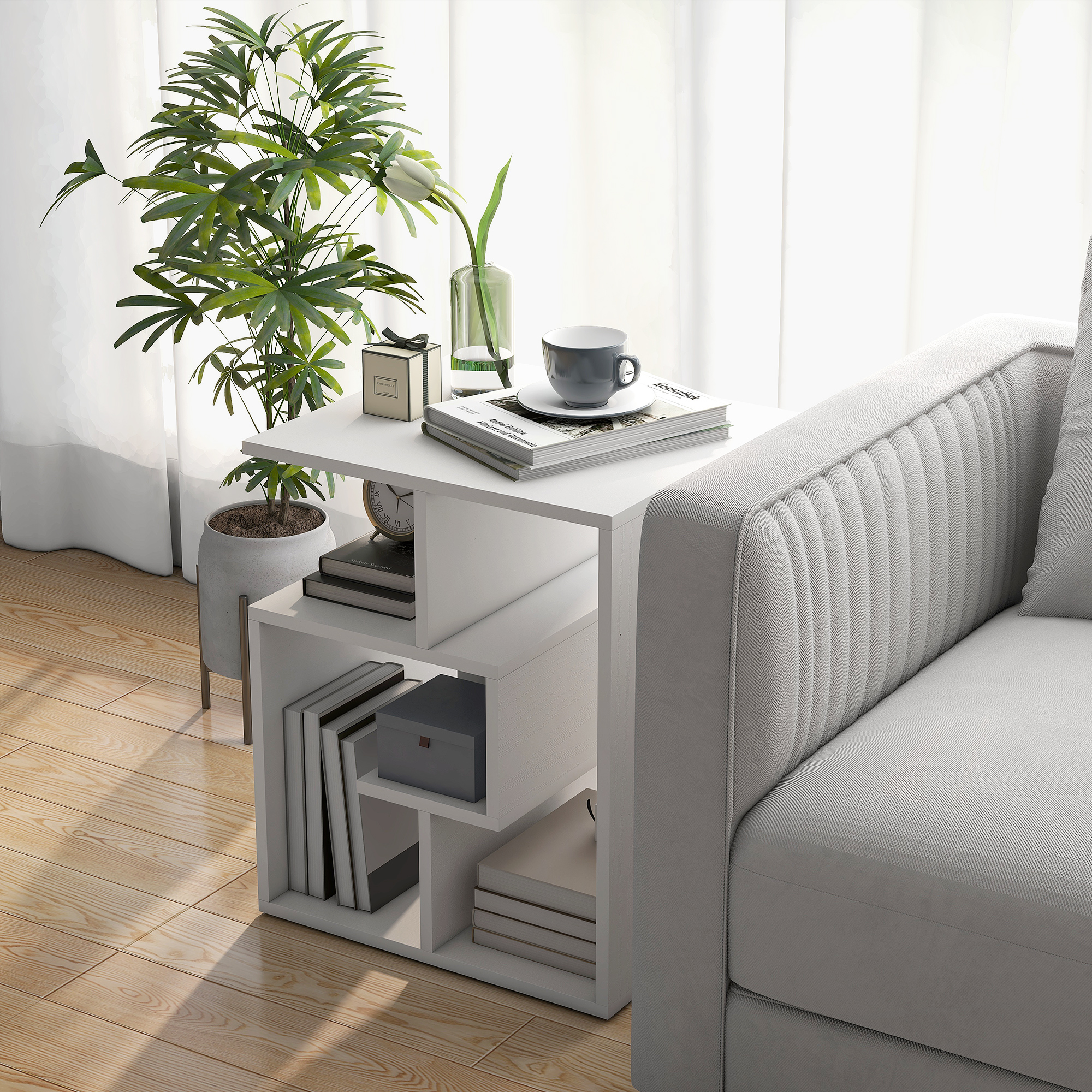 Una mesa auxiliar blanca con libros, una taza y una planta junto a un sofá.