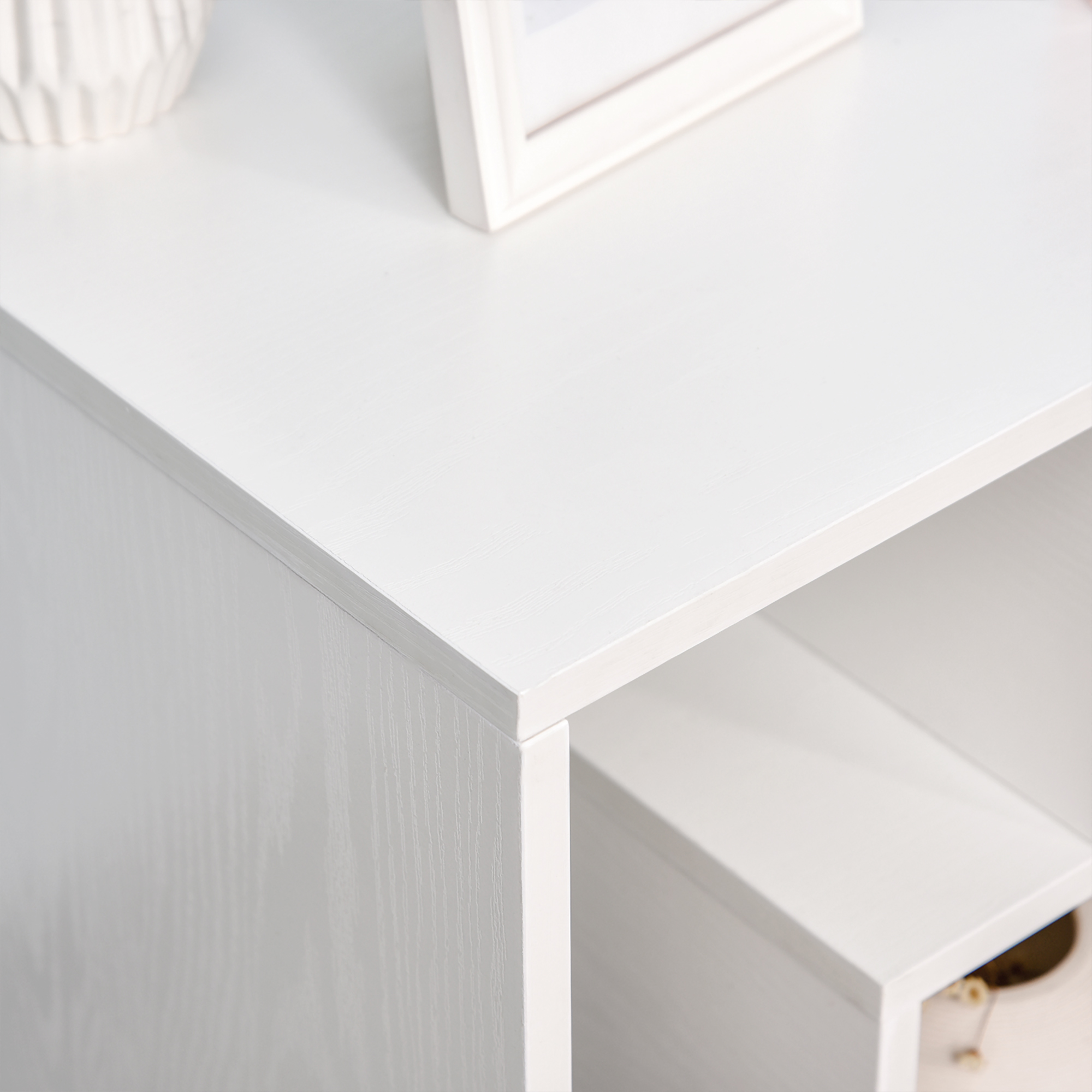 Muebles blancos de madera con estante y marco de fotos. Se ve un objeto de jarrón.