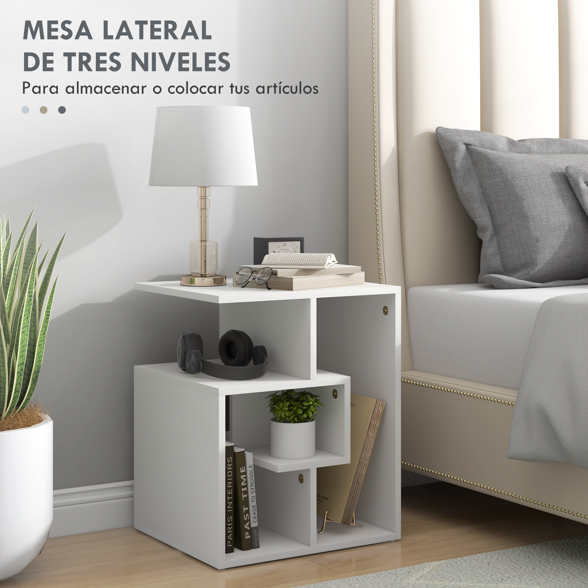 Una mesa auxiliar blanca de tres niveles junto a una cama con almohadas. Incluye lámpara y planta.