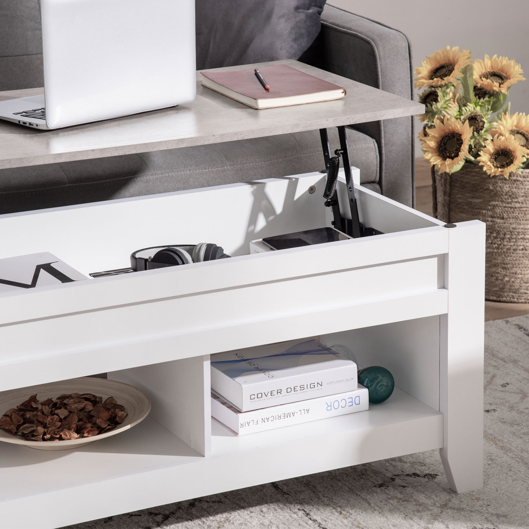 Una mesa de centro elevable con portátil, cuaderno, auriculares y una cesta de girasoles.