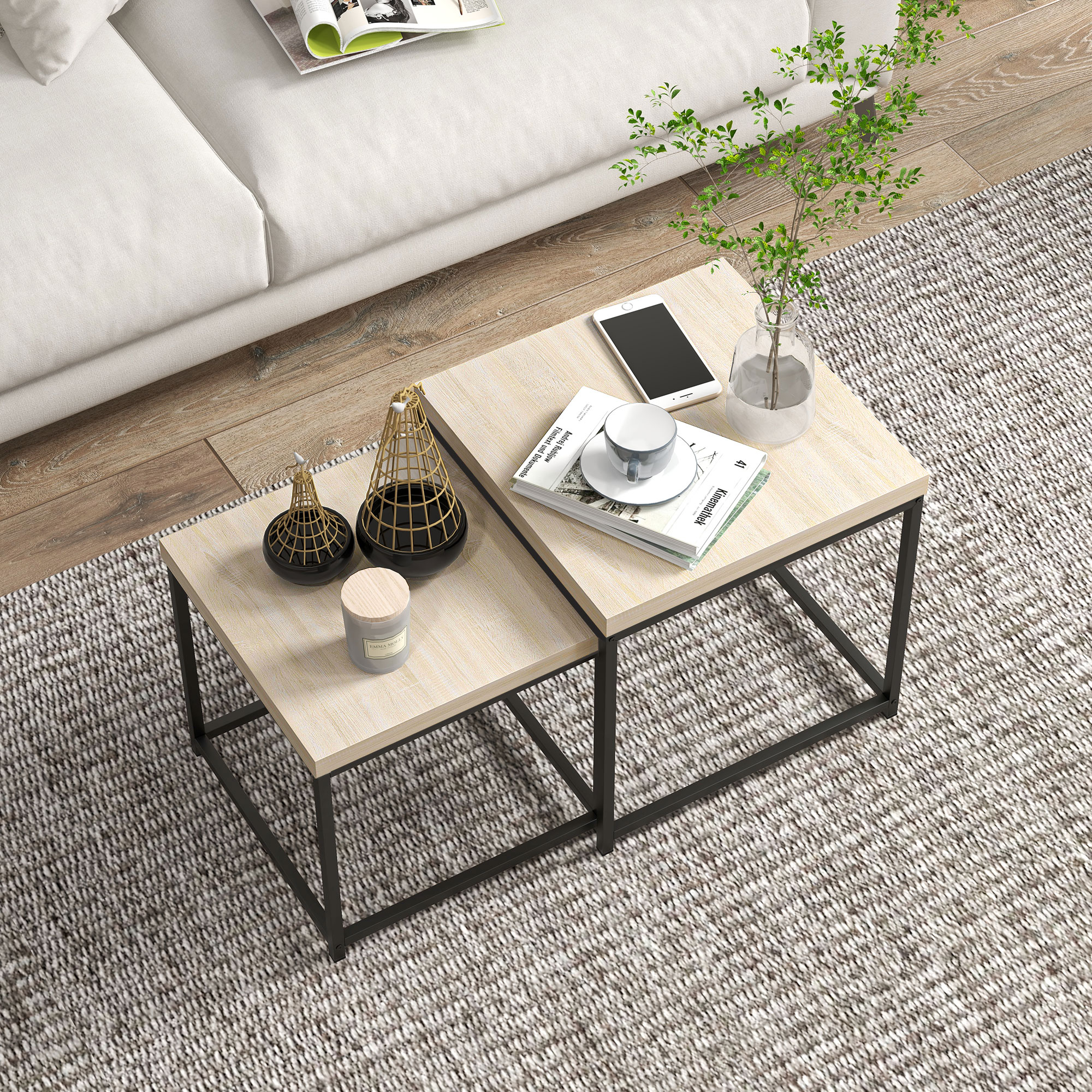 Dos mesas de madera con marcos de metal negro sobre alfombra. Tienen taza, móvil y decoración.