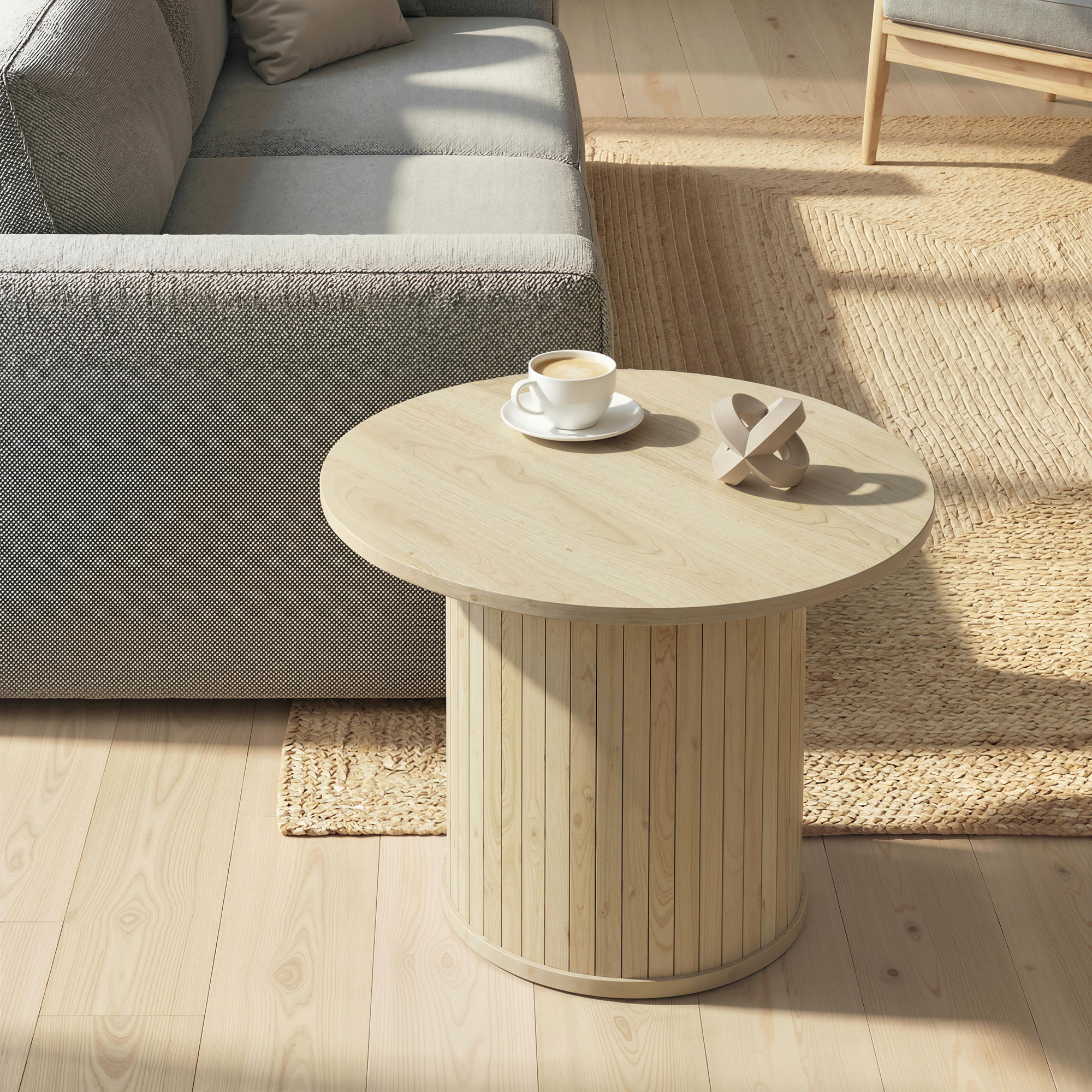 Una mesa de centro redonda de madera con una taza y decoración al lado de un sofá.