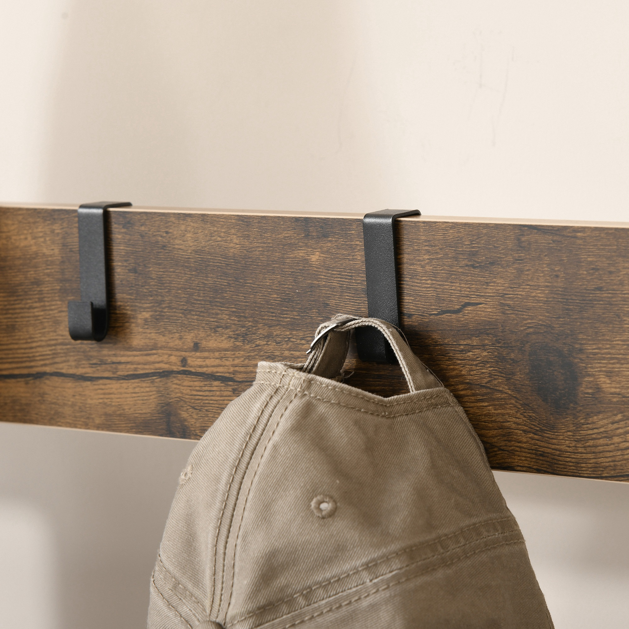 Un sombrero beige cuelga de una tabla de madera con dos ganchos negros.