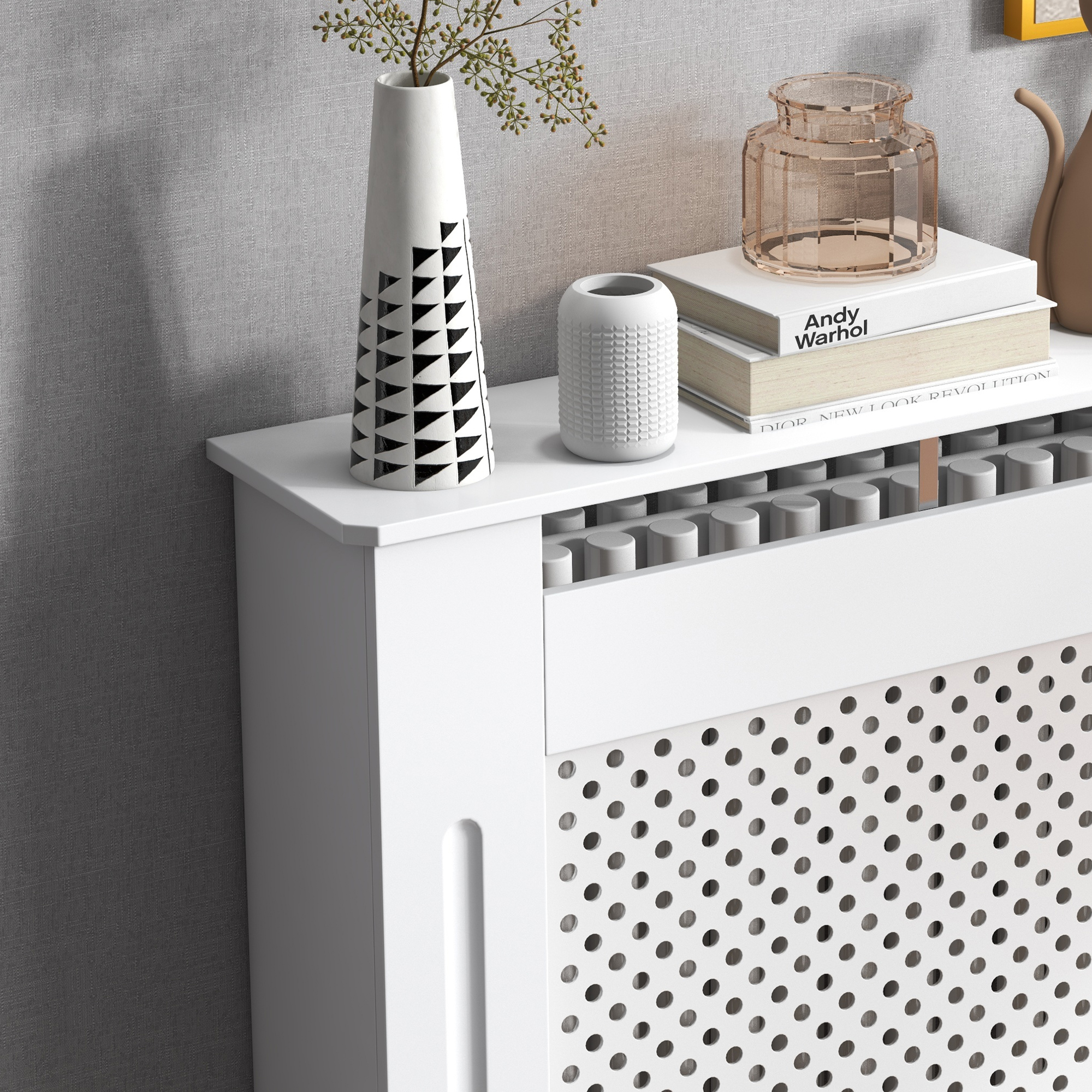 Una cubierta de radiador blanca con jarrones y libros decorativos.