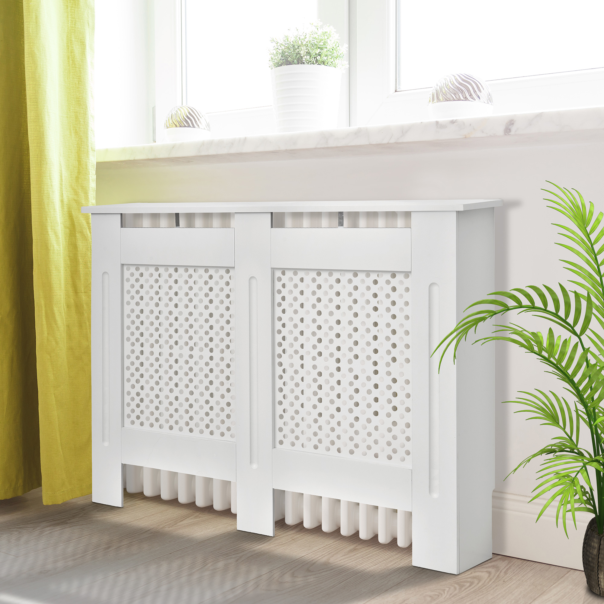 Un mueble blanco para radiador con frontal perforado se sitúa frente a una ventana.