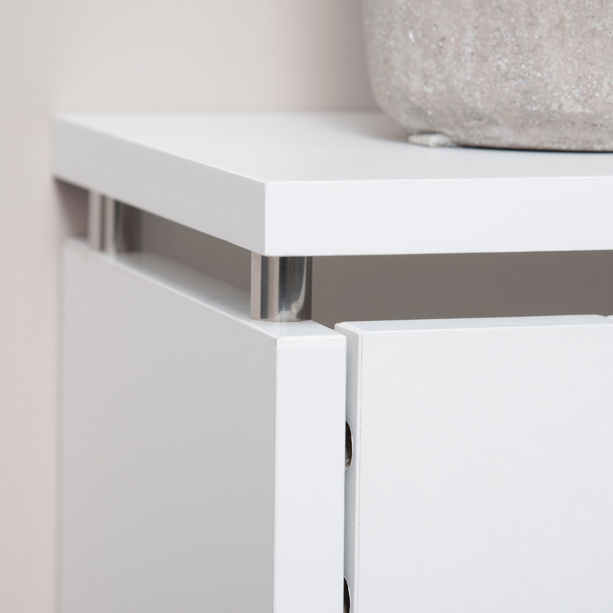 Cómoda blanca con soportes plateados y una maceta gris.