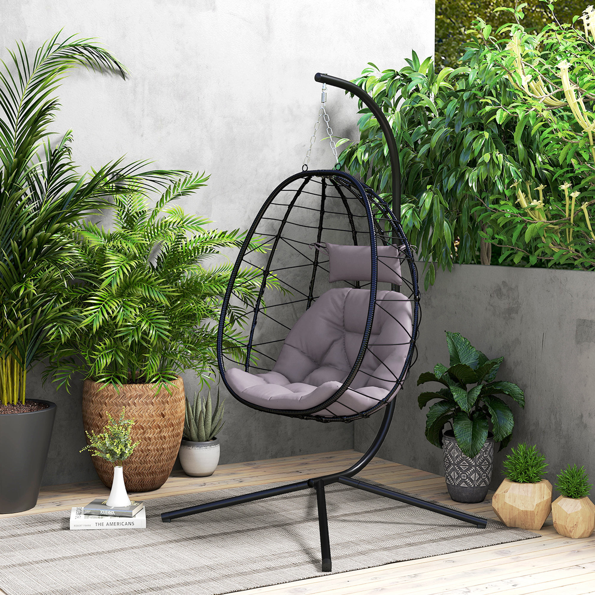 Una silla colgante de huevo negra con cojines grises, rodeada de plantas verdes.