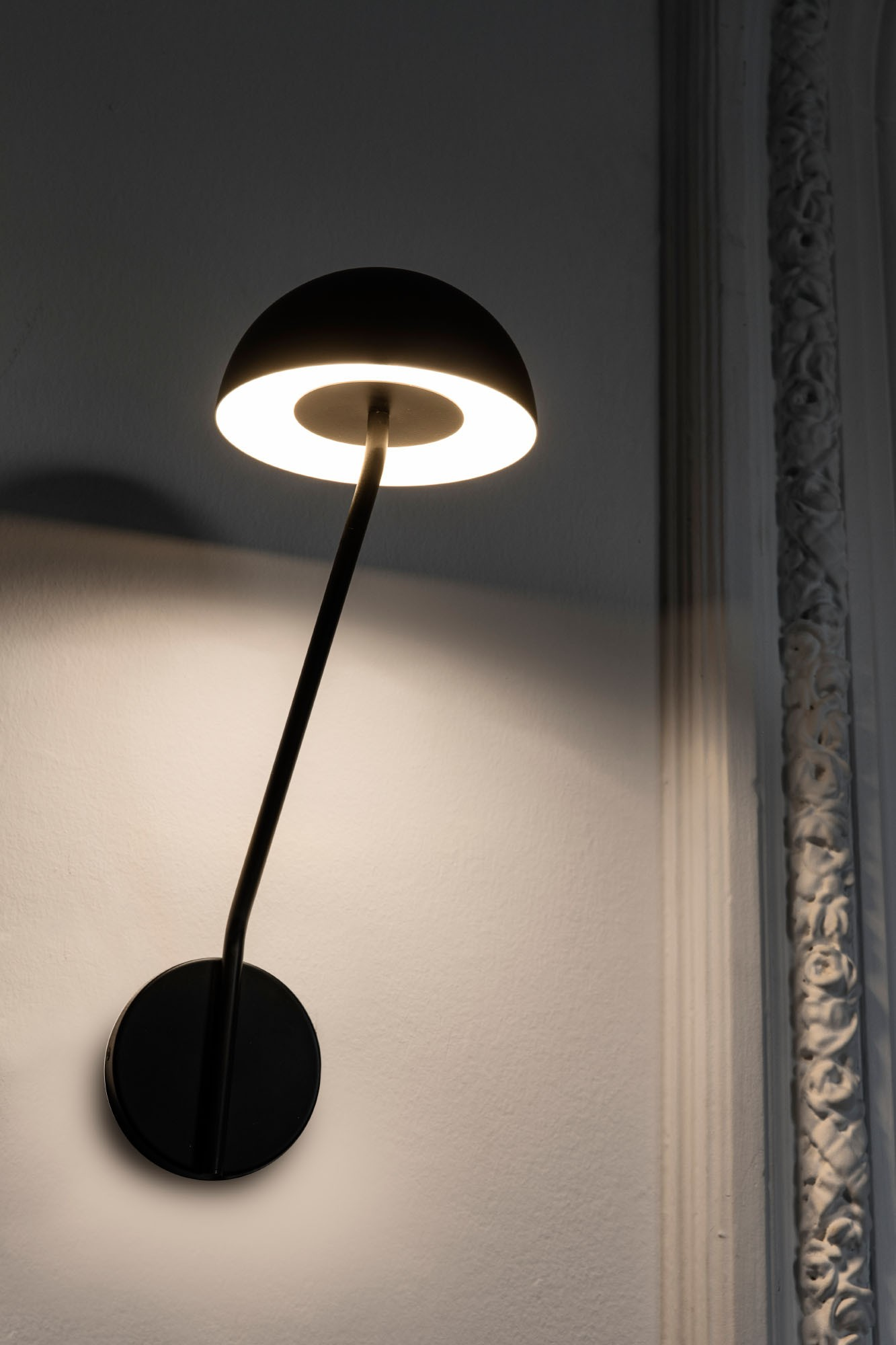 Lampada da parete nera con paralume rotondo che emette luce calda.