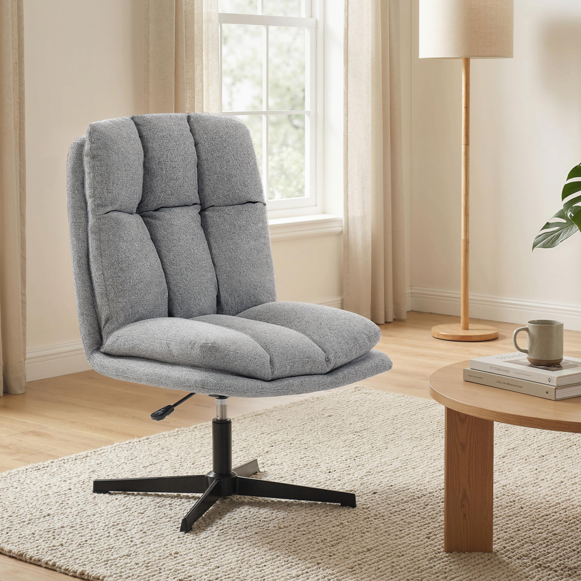 Silla tapizada gris con base ajustable sobre alfombra crema, junto a una mesa redonda de madera.