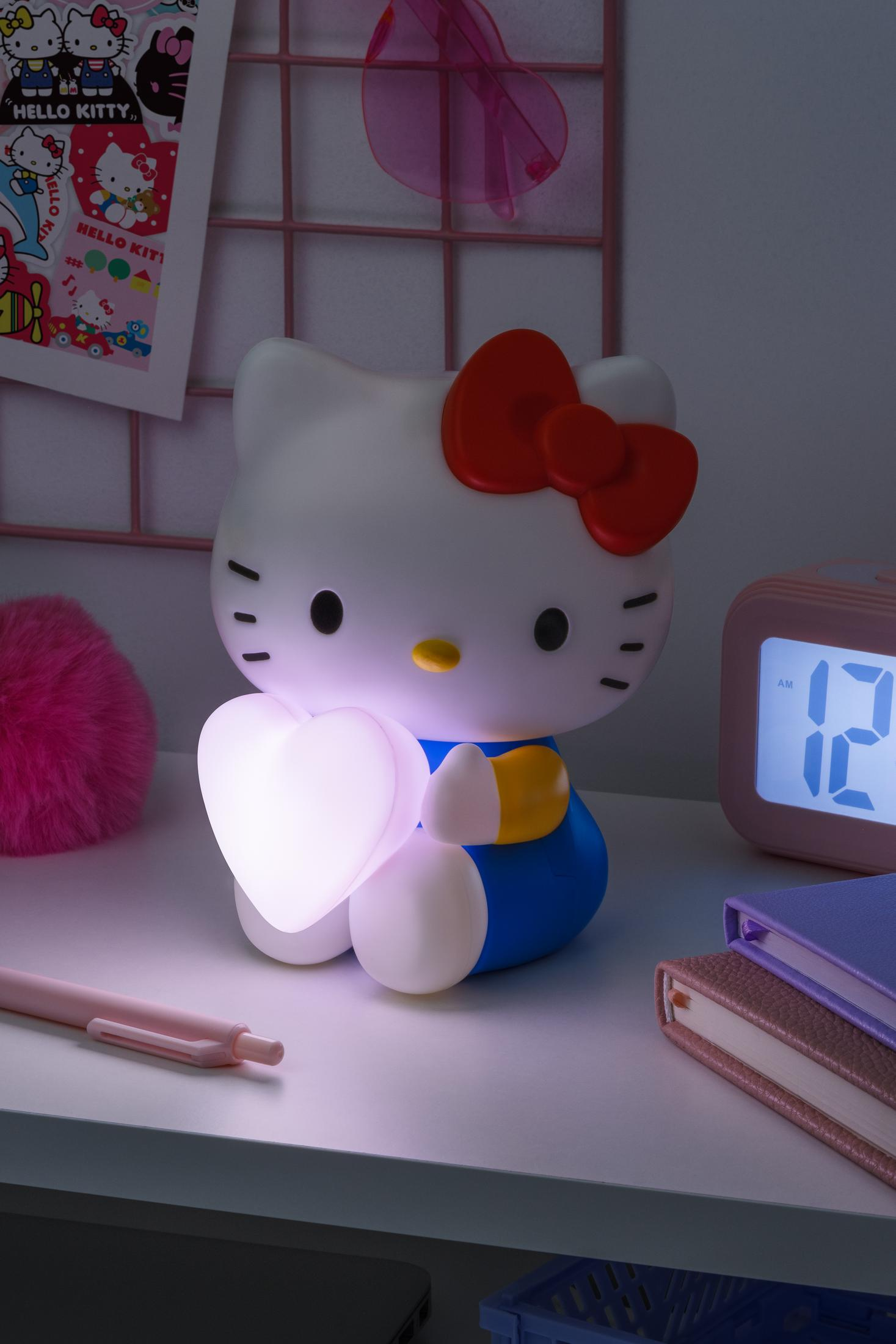 Biała lampka Hello Kitty ze świecącym sercem stoi na biurku z różowym długopisem.