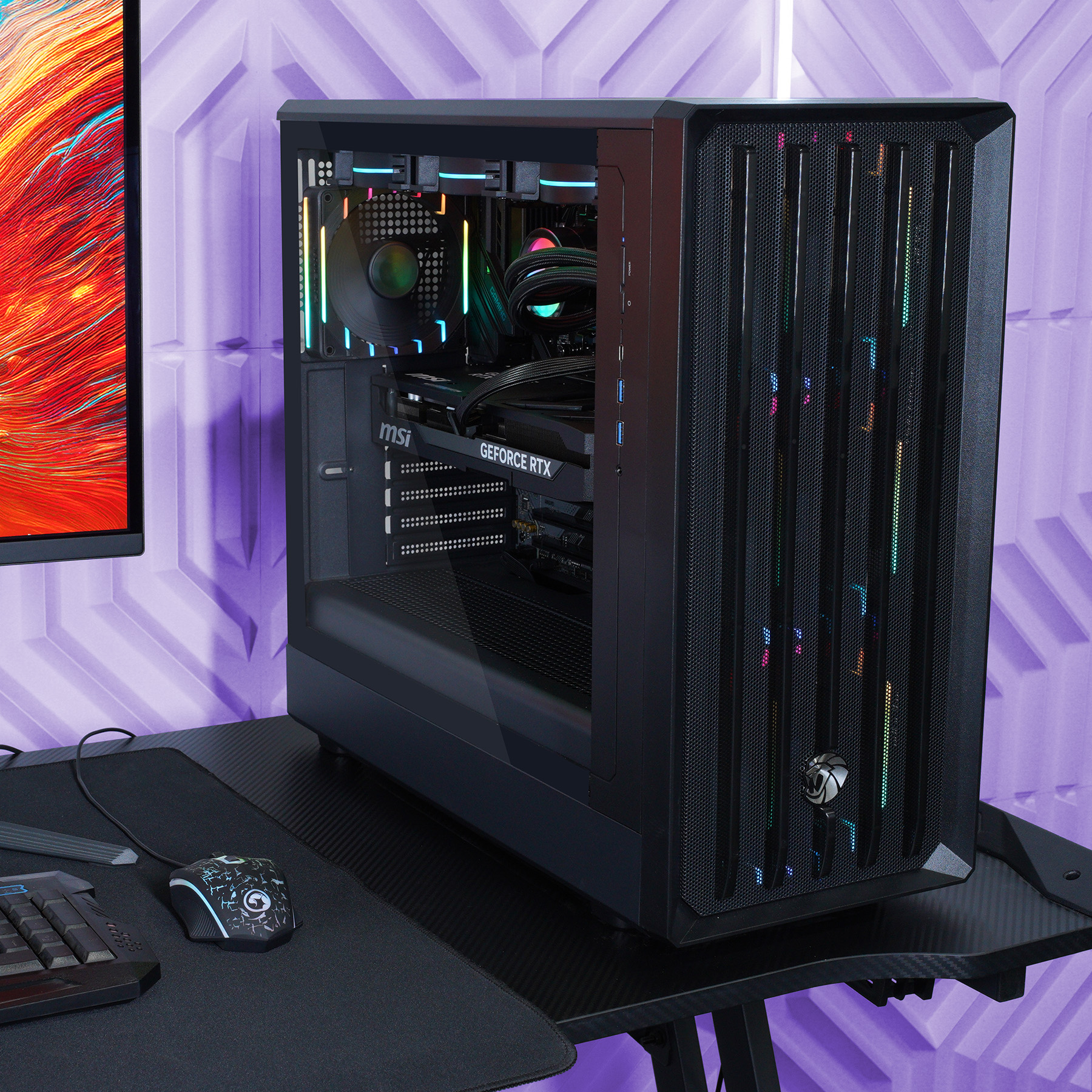 Ein schwarzer PC-Tower mit RGB-Beleuchtung steht auf einem Schreibtisch neben einem Monitor.