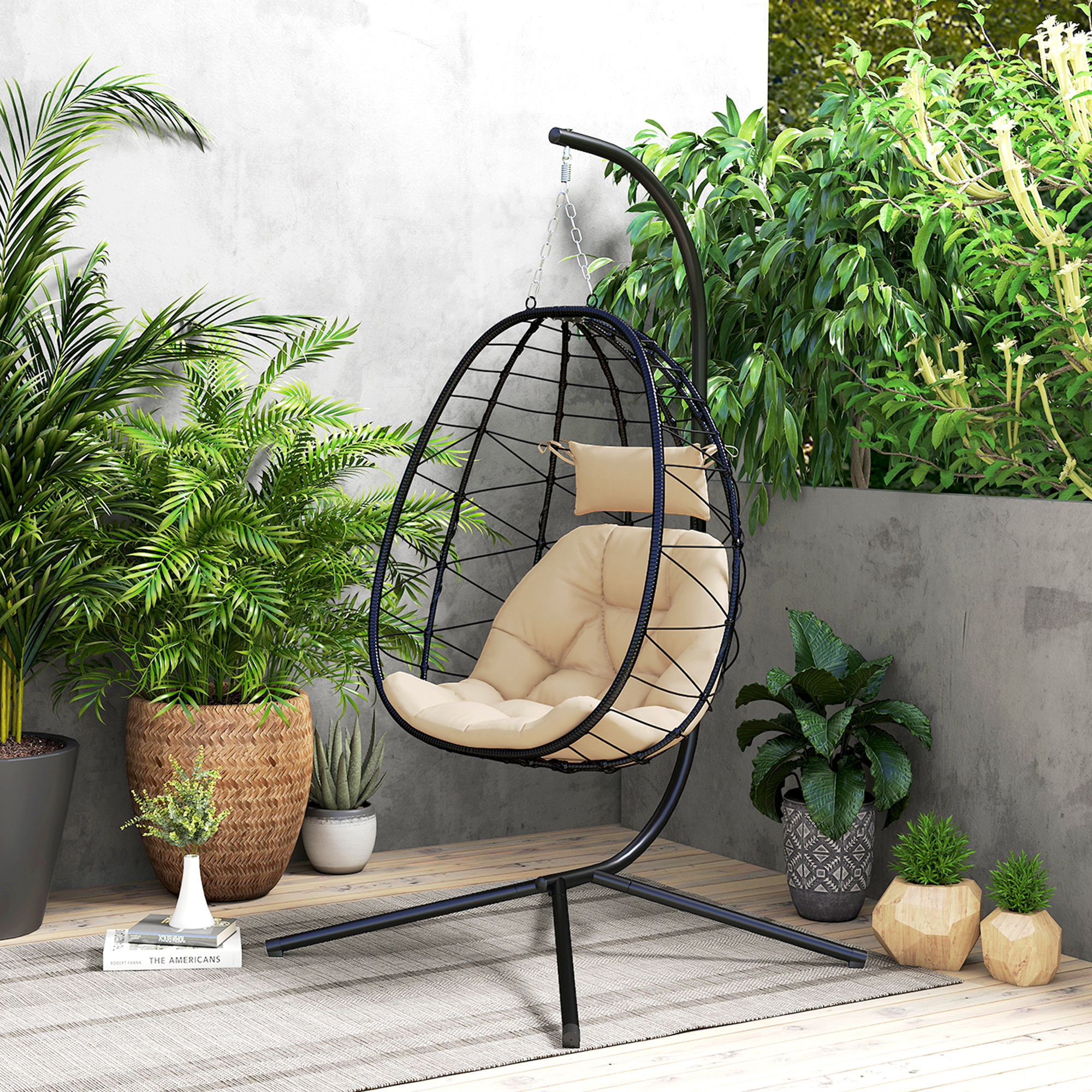 Una silla colgante de mimbre negra con cojines beige está en un patio.
