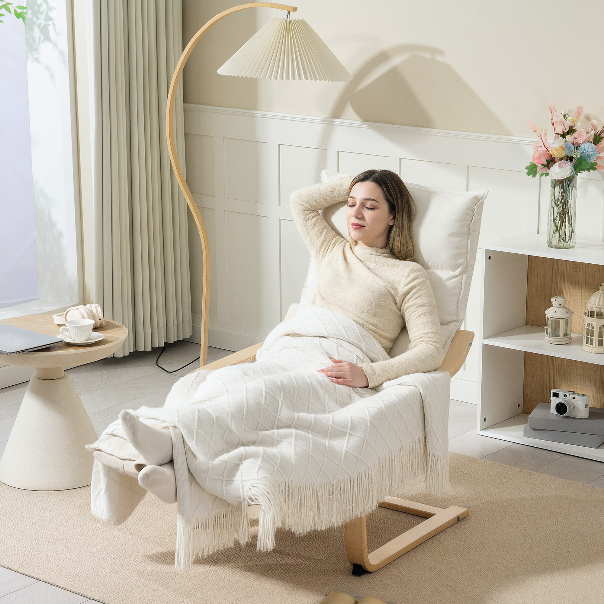 Una mujer se relaja en un sillón bajo una manta, junto a una mesa con portátil y taza.