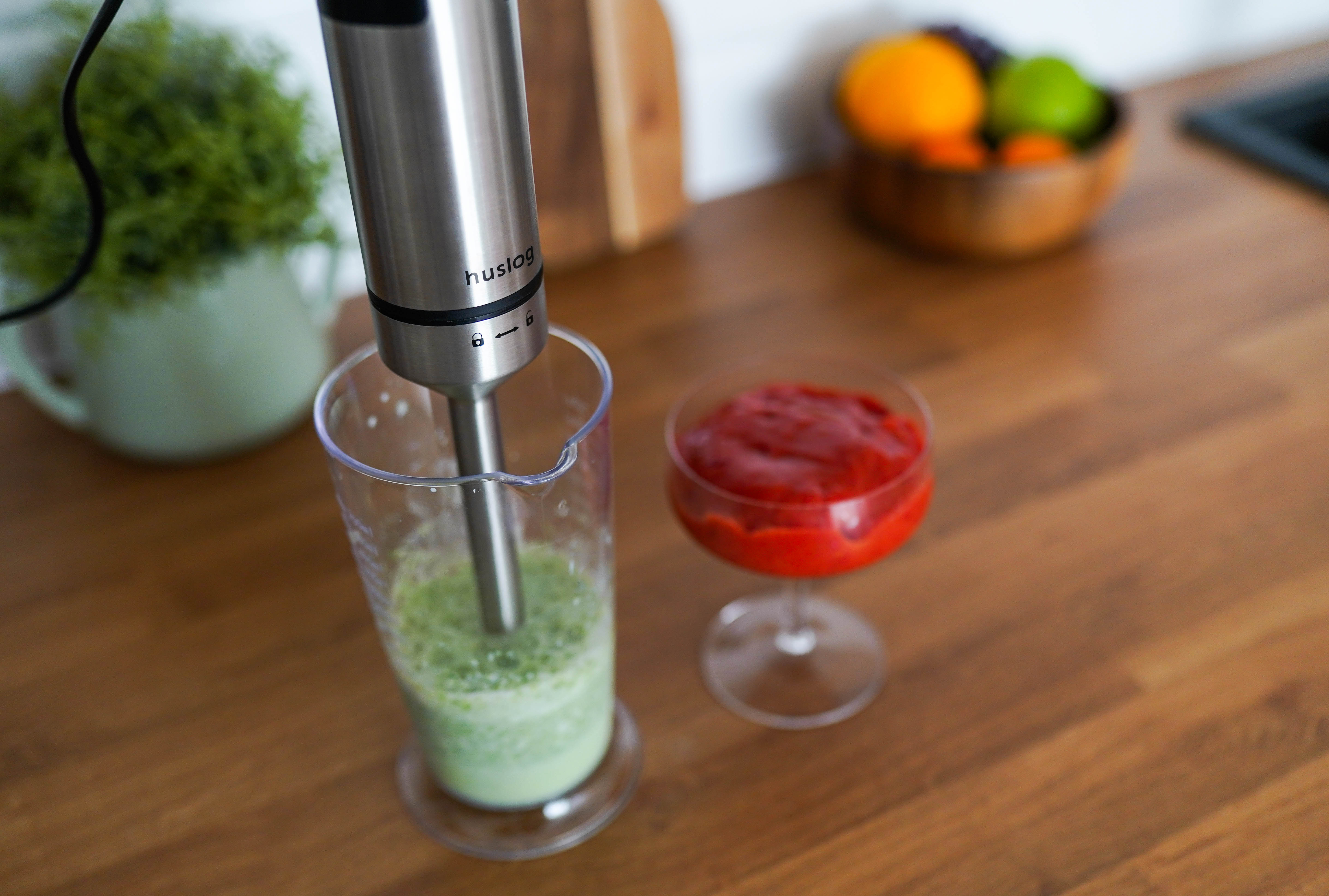 Blender ręczny miesza zielony płyn w kubku miarowym obok szklanki z czerwonym puree.