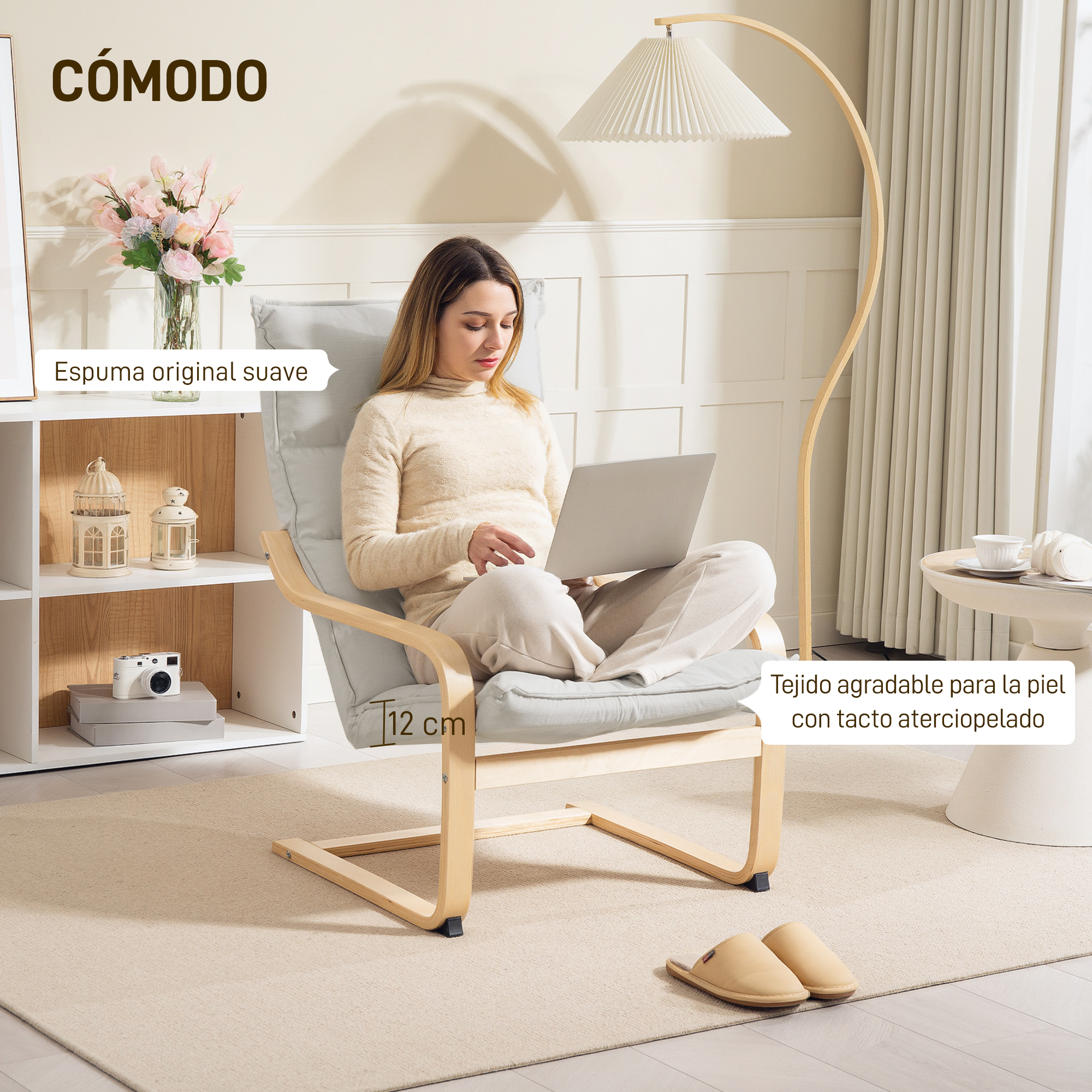 Mujer sentada en silla con portátil. Flores, lámpara y mesa auxiliar al fondo.