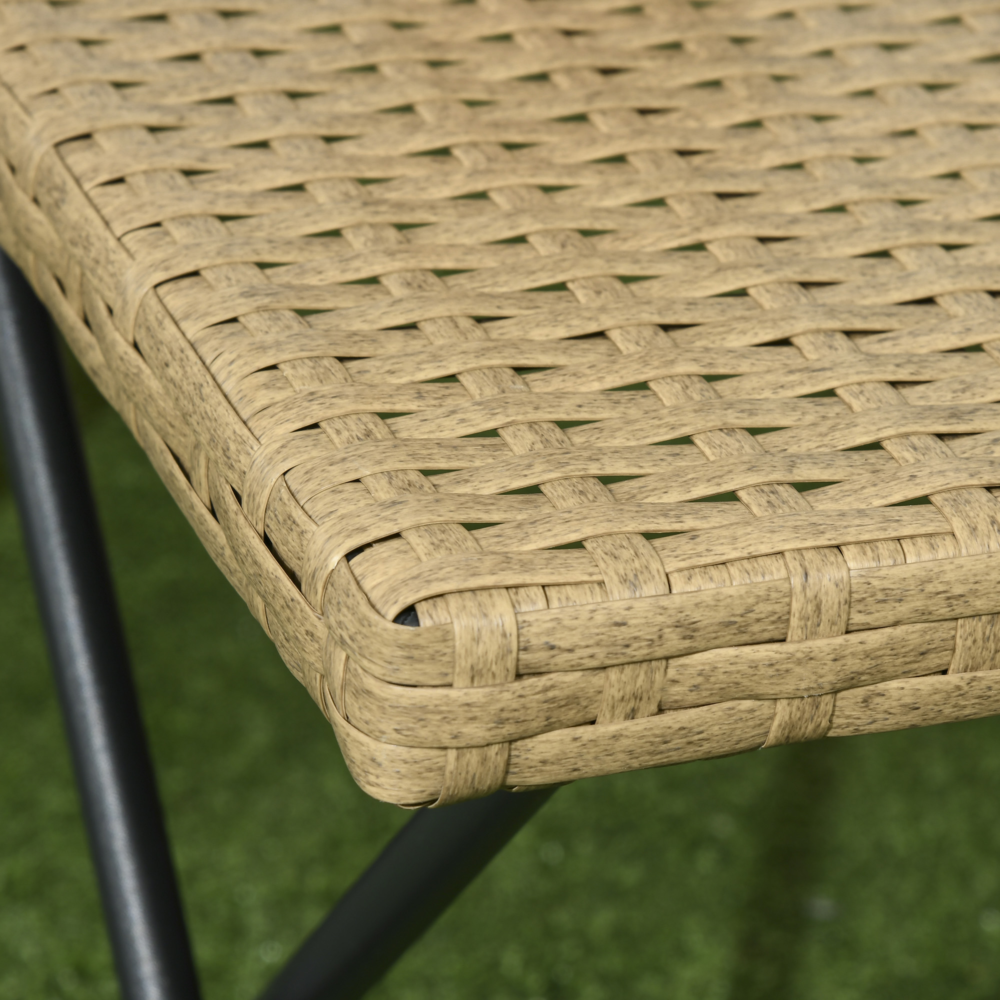 Primo piano di un piano tavolo in rattan marrone con telaio in metallo nero su erba verde.