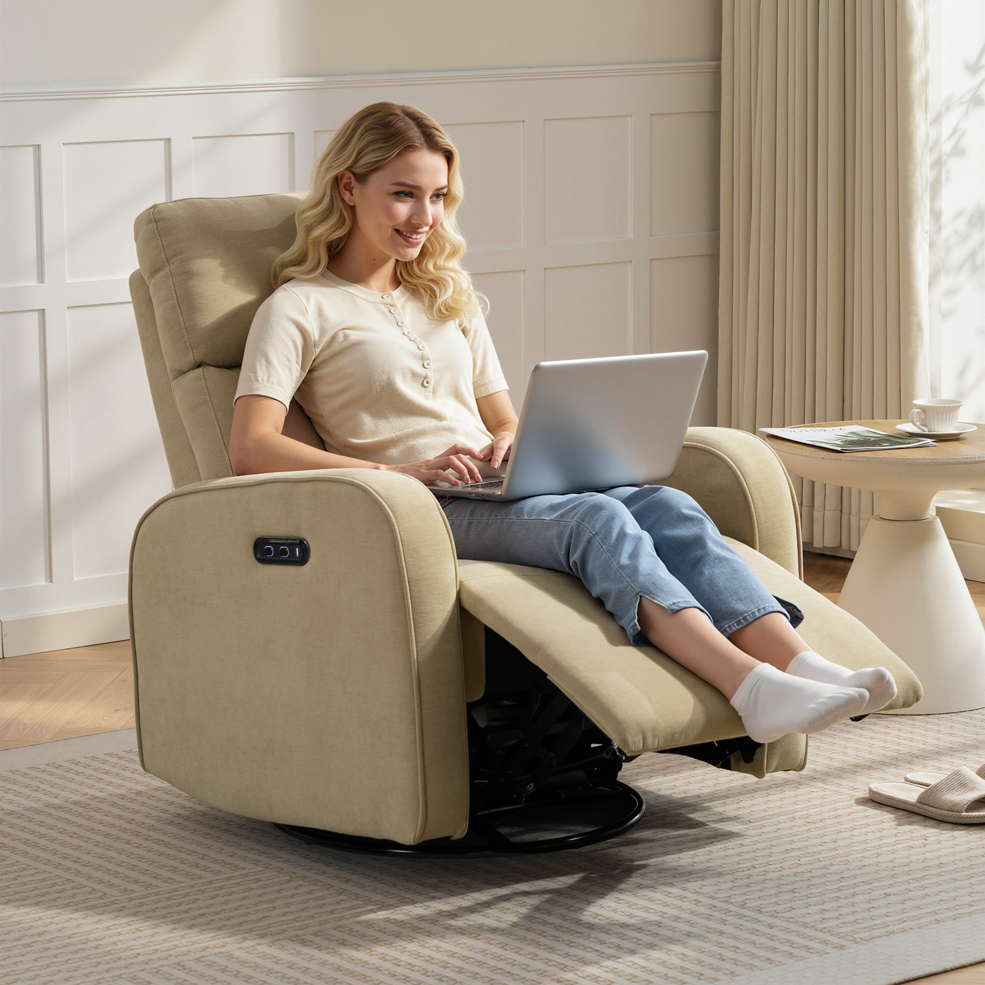 Una mujer sentada en un sillón reclinable beige usando una laptop. Hay una mesita auxiliar cerca.