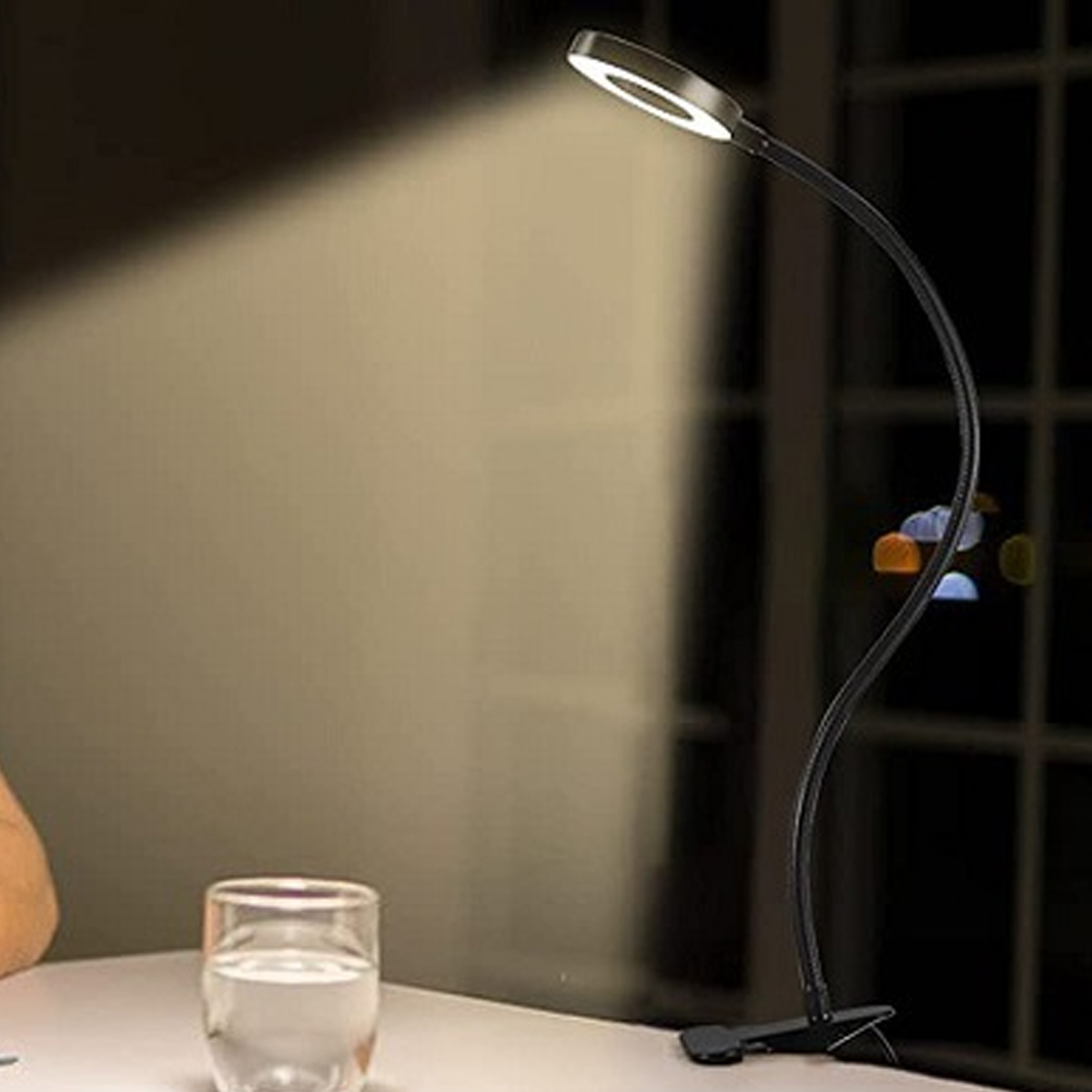 Eine schwarze Schreibtischlampe mit Ringlicht und Klemme leuchtet auf einem Schreibtisch.