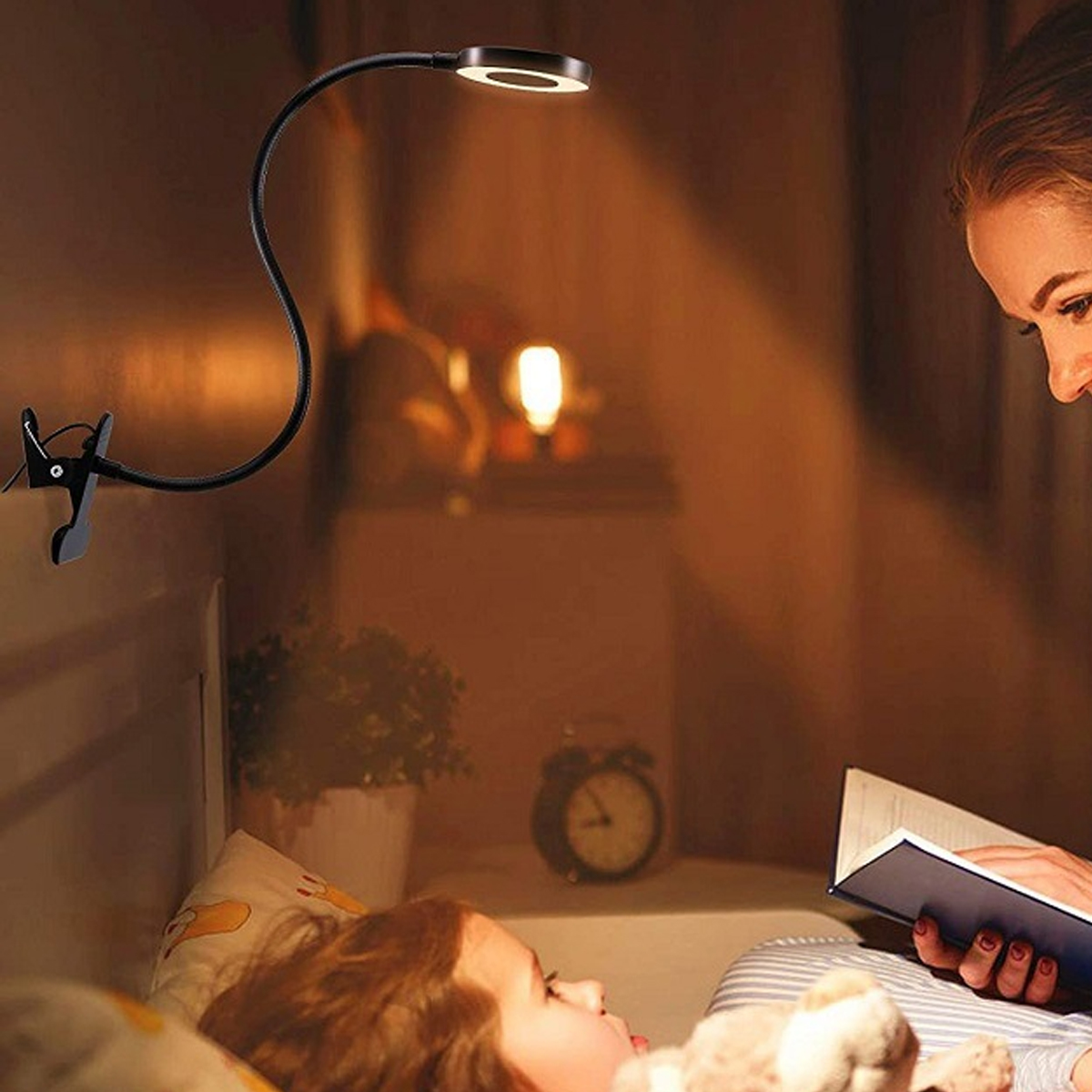 Eine Frau liest einem Kind im Bett eine Gute-Nacht-Geschichte vor, beleuchtet von einer Klemmleuchte.