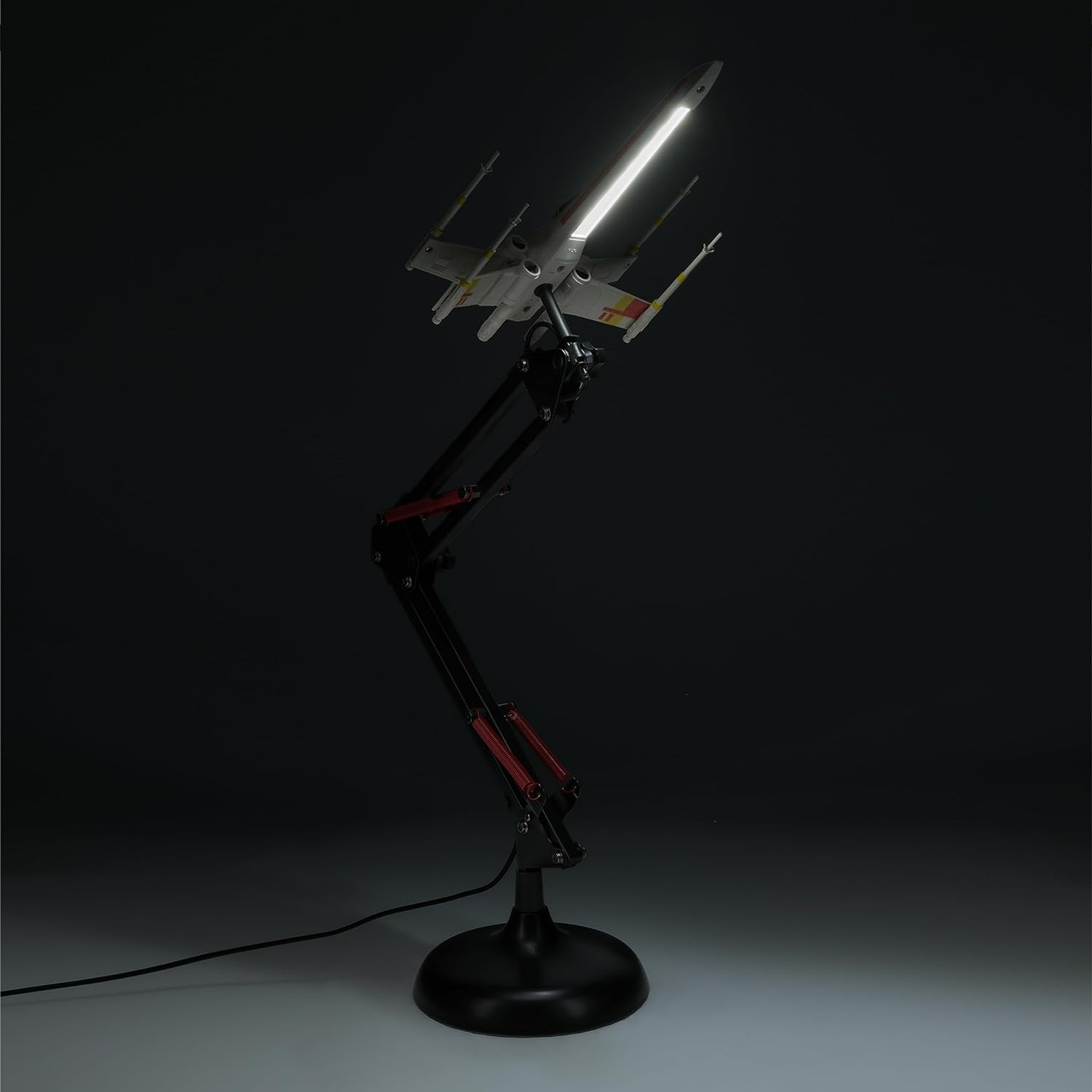 Biały model X-wing z czerwonymi oznaczeniami, oświetlony jasnym paskiem LED.