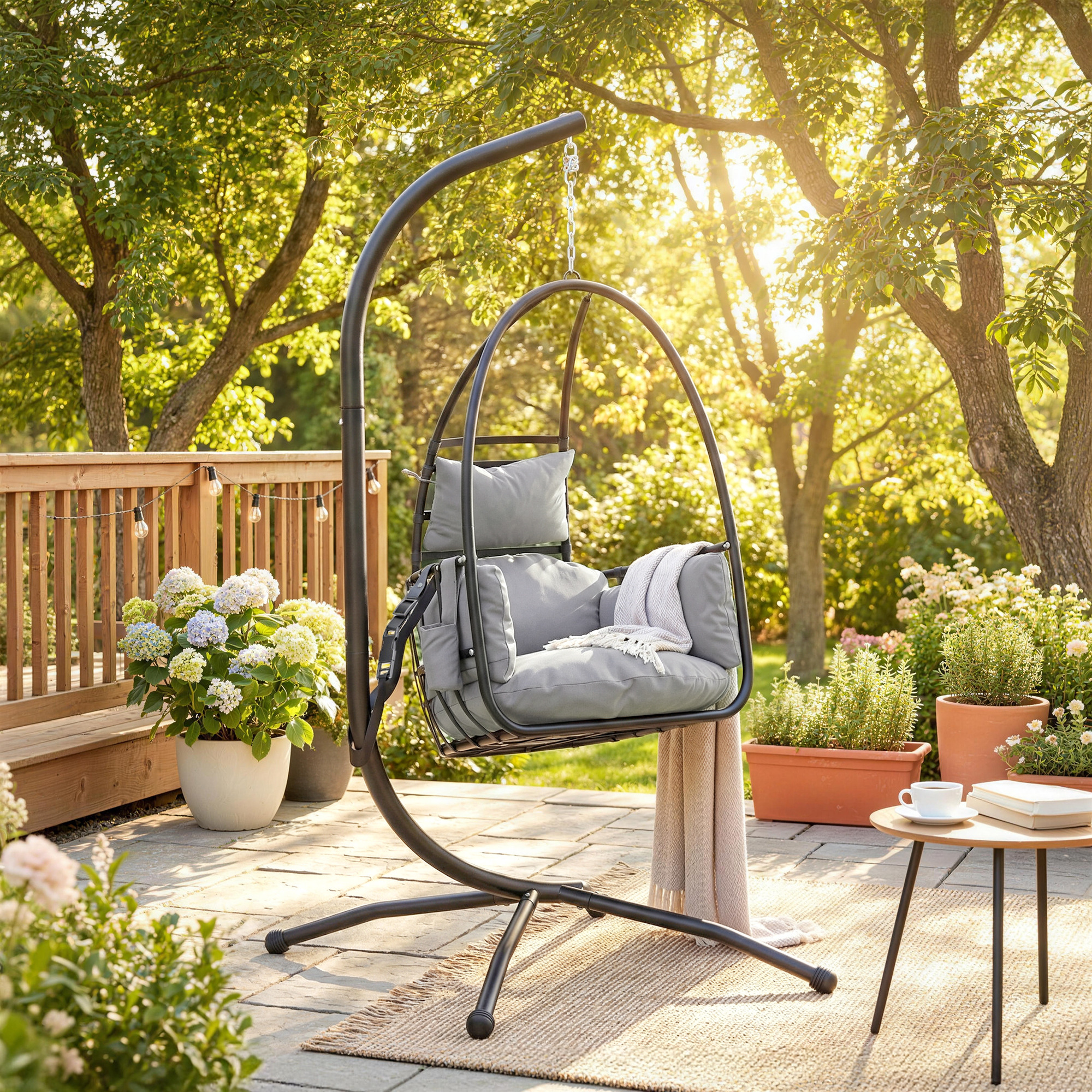 Una silla colgante de huevo gris con cojines se encuentra en un patio junto a plantas.