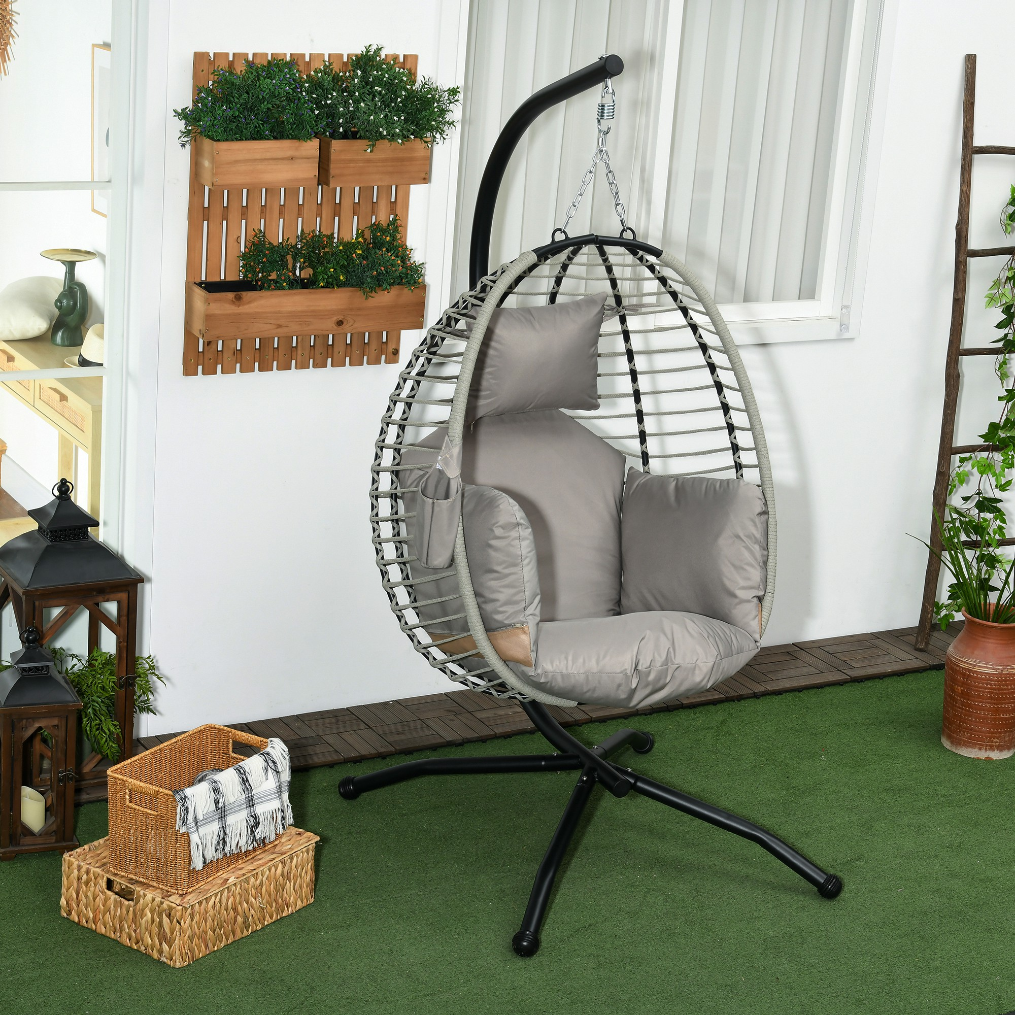 Una silla colgante con cojines grises se asienta sobre césped artificial verde.