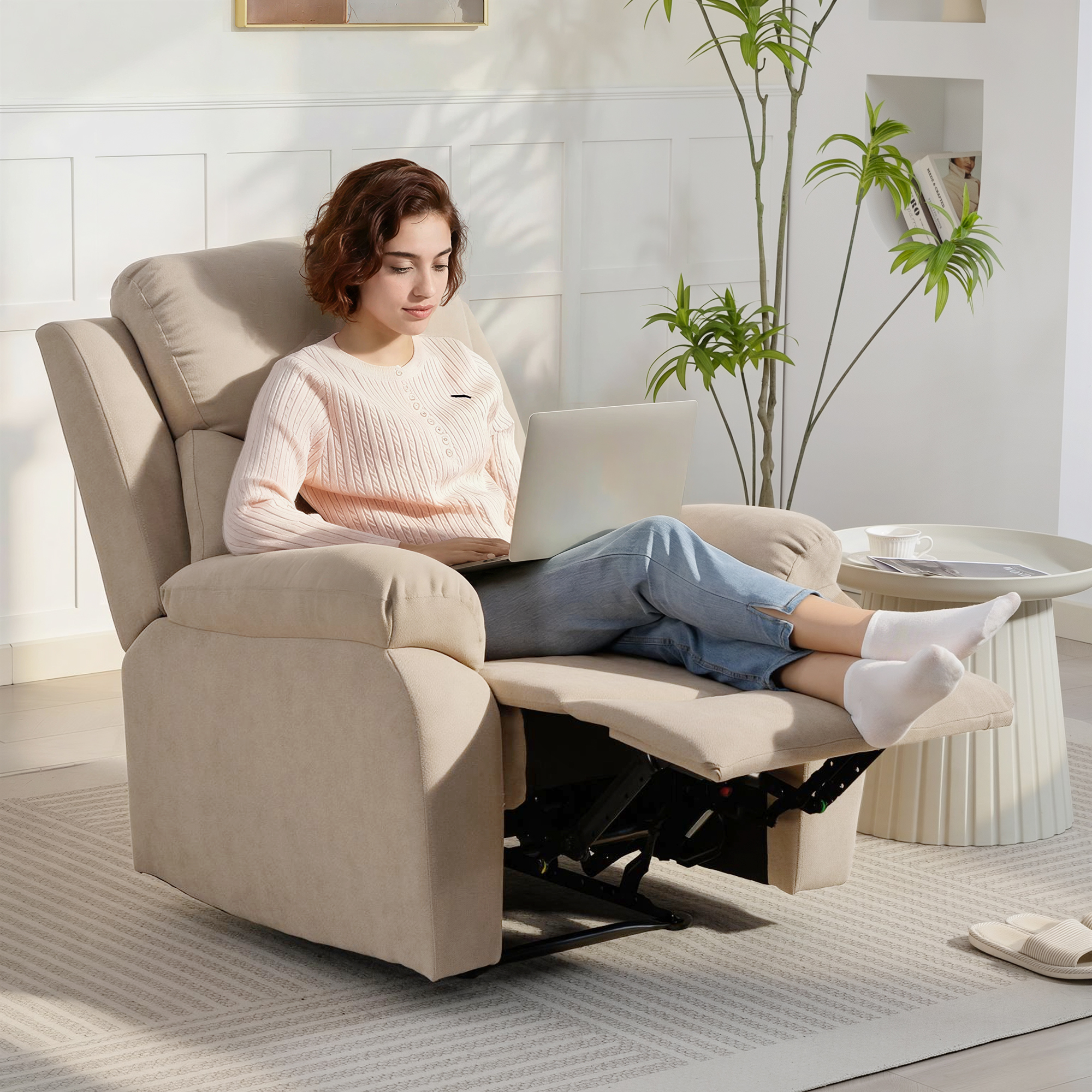 Una mujer se sienta en un sillón reclinable beige, trabajando en un portátil. Su reposapiés está extendido.