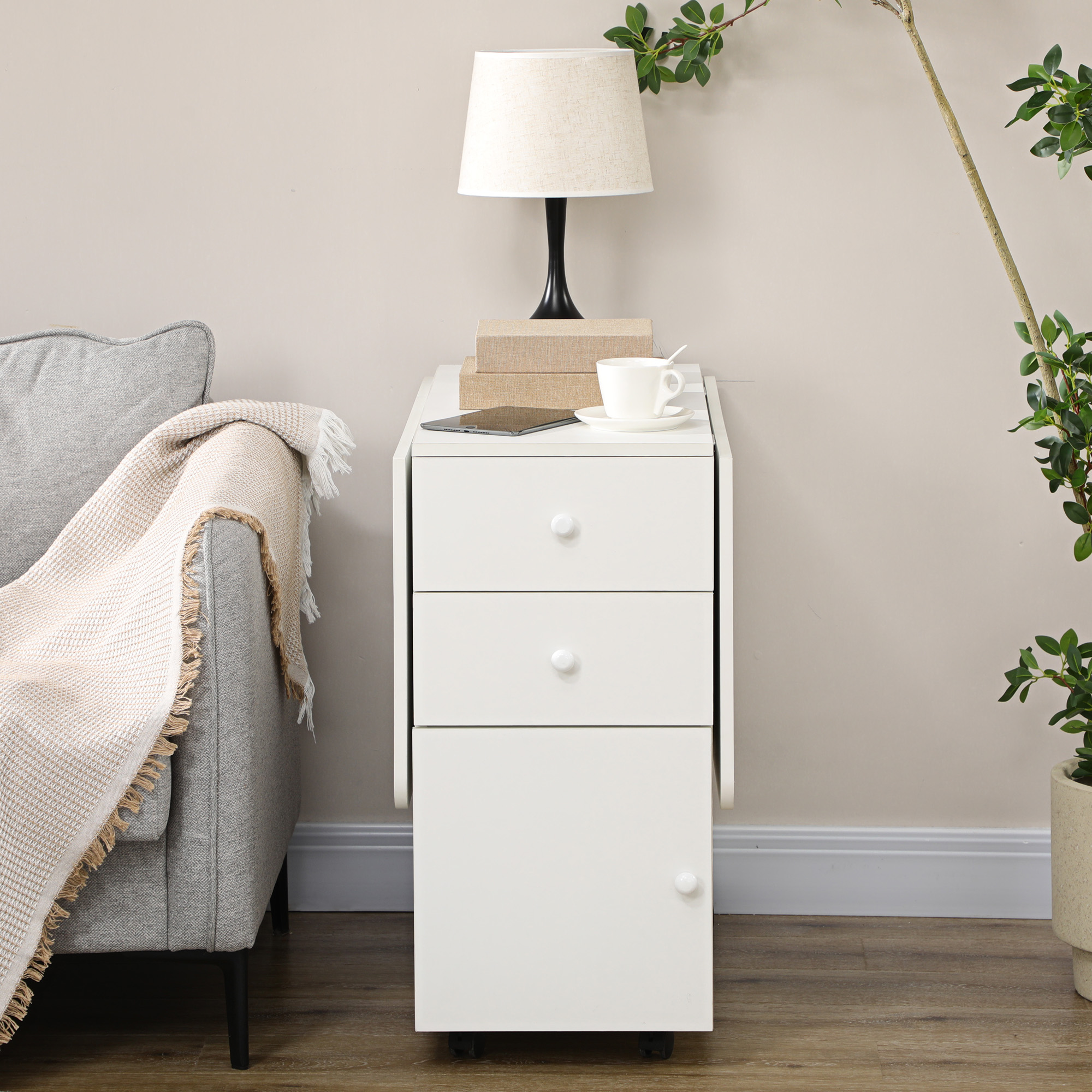 Un mueble blanco con tres cajones junto a un sofá gris con manta.