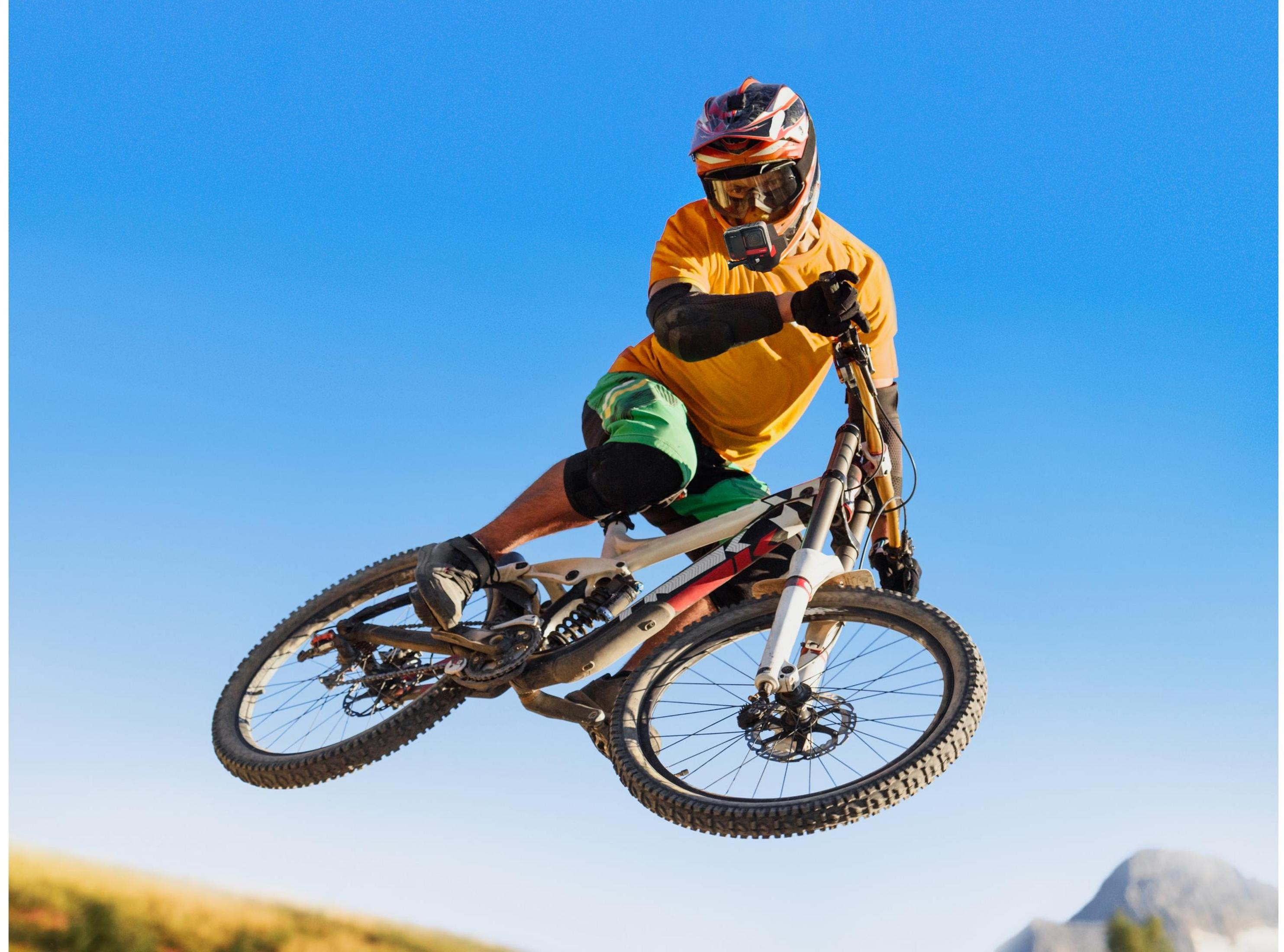Ein Mountainbiker springt mit einem gelben T-Shirt und Helm in der Luft.