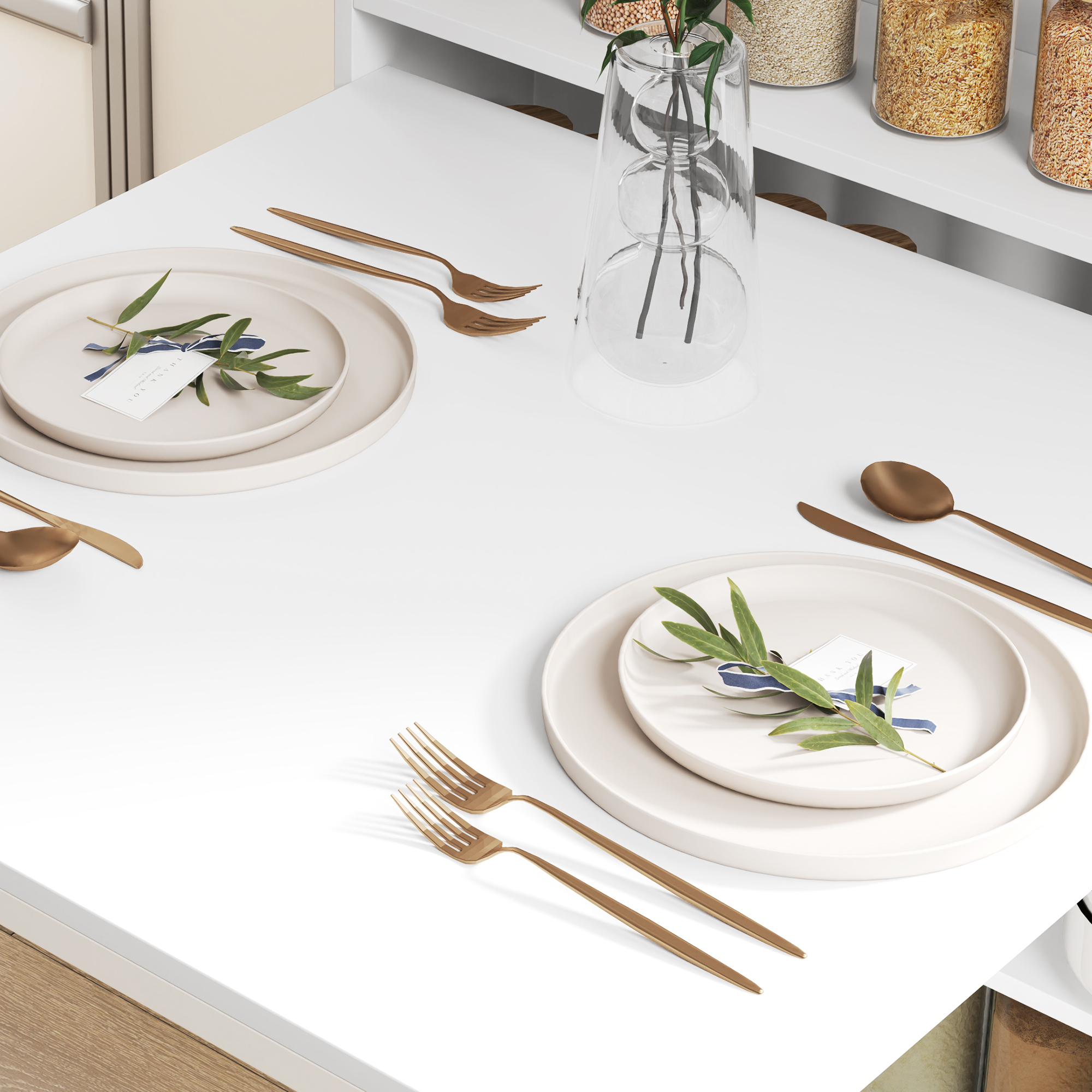 Dos servicios de mesa con cubertería dorada y vegetación sobre una mesa blanca.