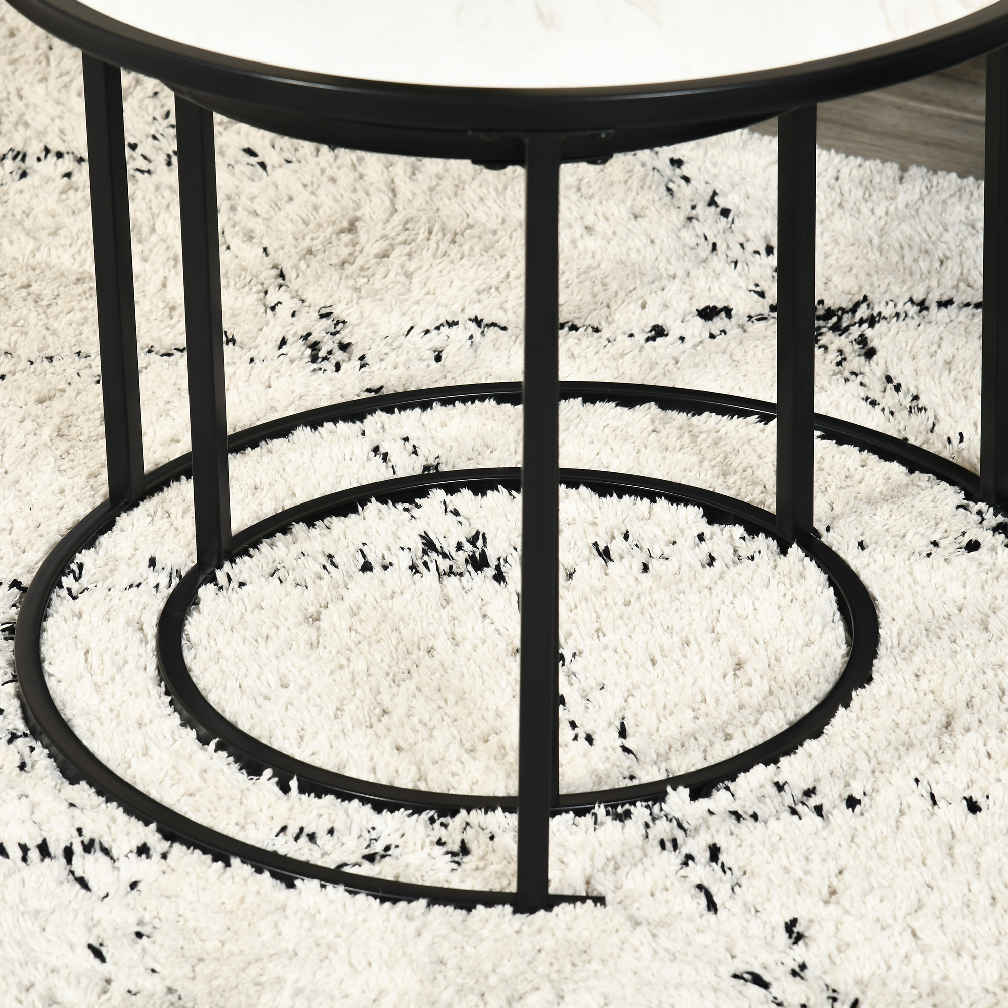 Una mesa de centro redonda con tapa de mármol y patas de metal negro sobre alfombra.