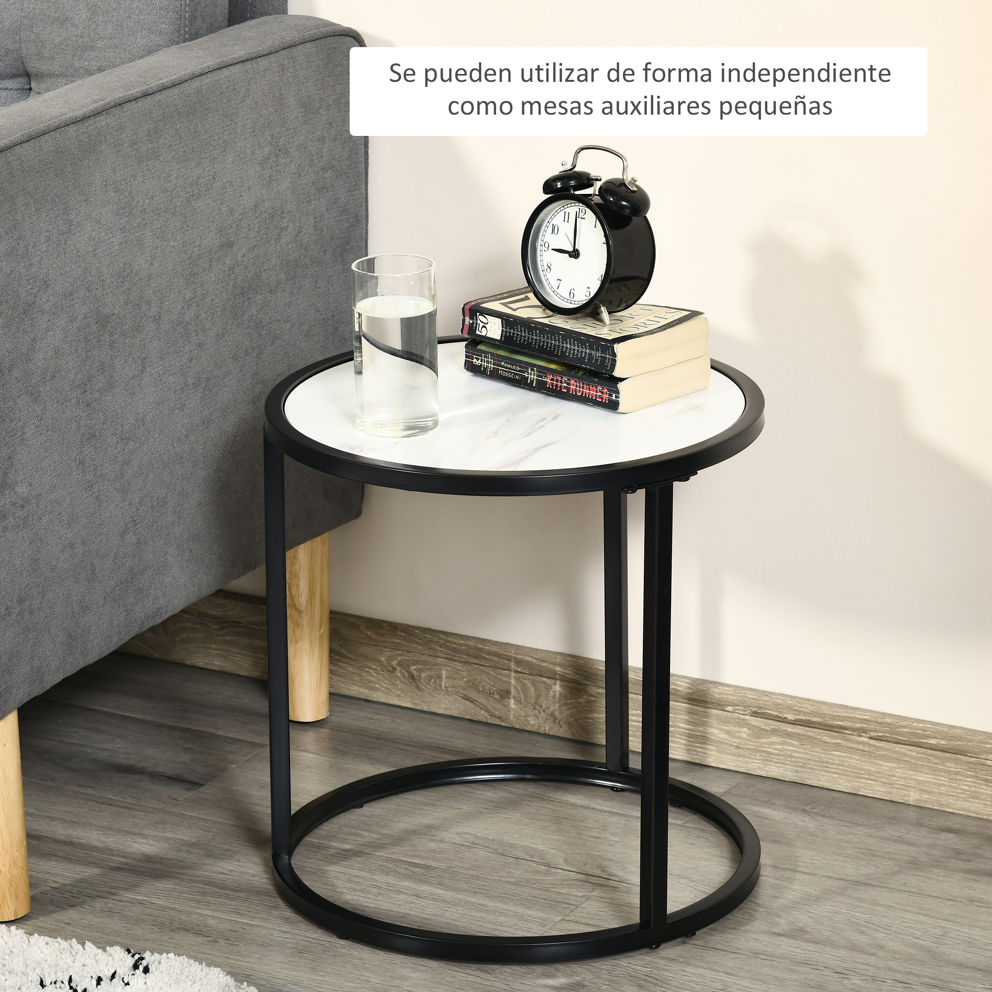 Una mesita auxiliar con tapa de mármol, libros y despertador junto a un sofá.