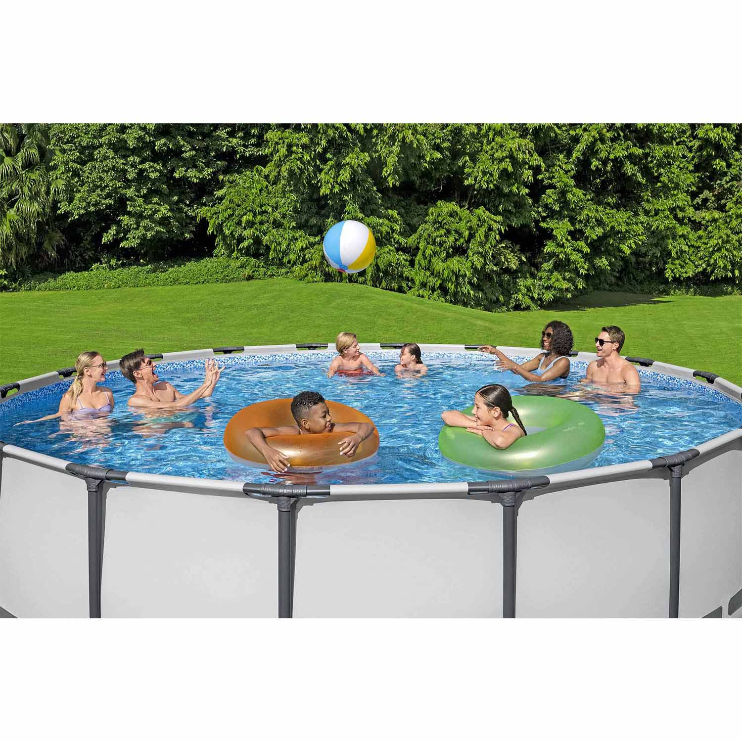 Ludzie pluskają się w basenie, chłopiec pływa w pomarańczowym kole, dziewczynka w zielonym.